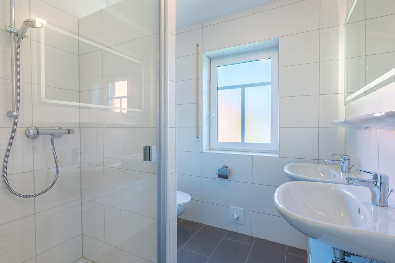 Badezimmer mit Dusche, zwei Waschbecken und Fenster.
