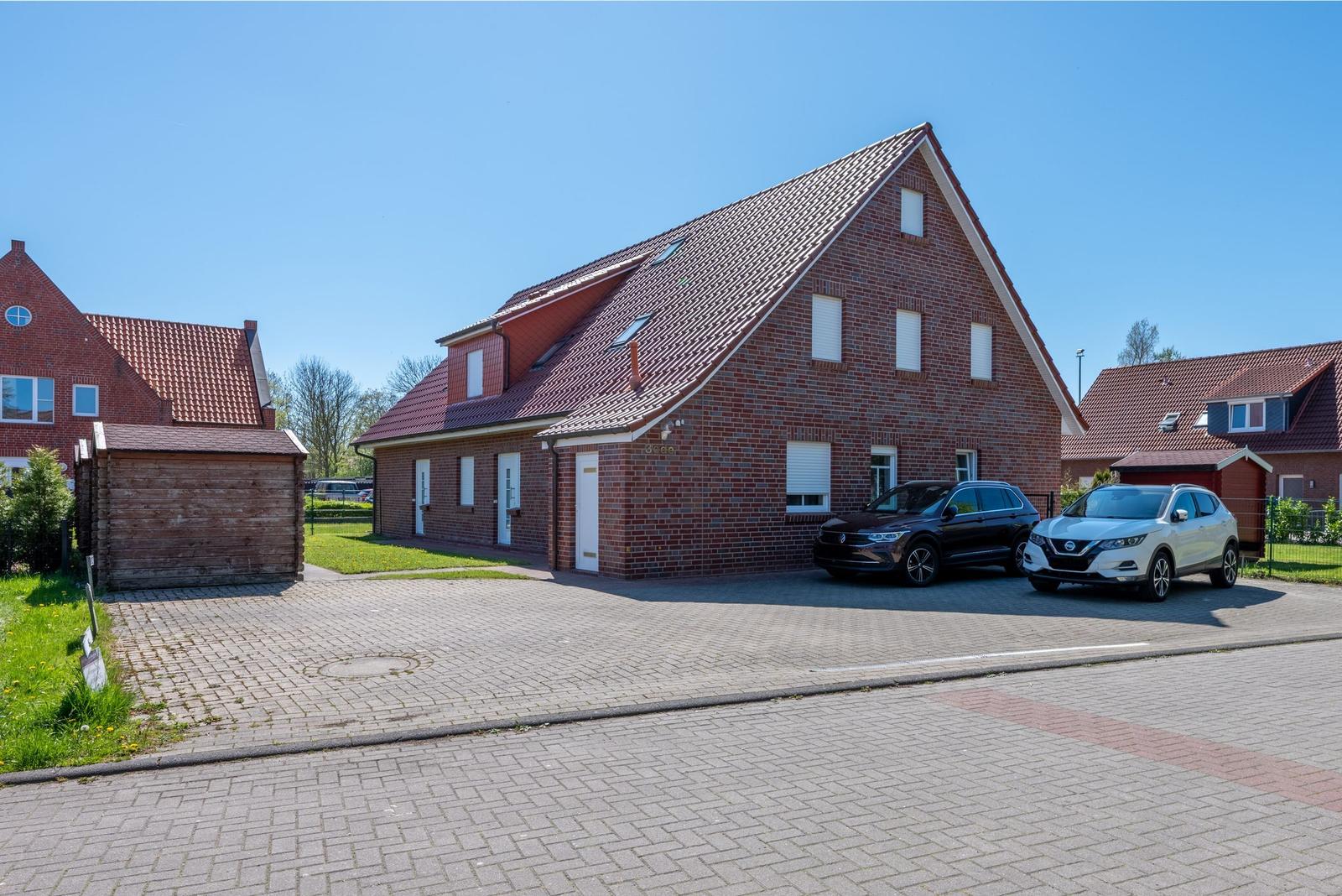 Rotes Backsteingebäude mit Dach und zwei parkenden Autos.