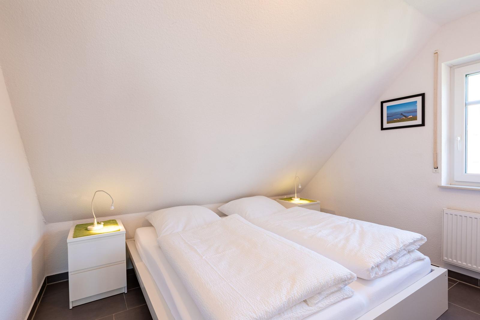 Schlafzimmer mit Doppelbett, zwei Nachttischen und Fenster.