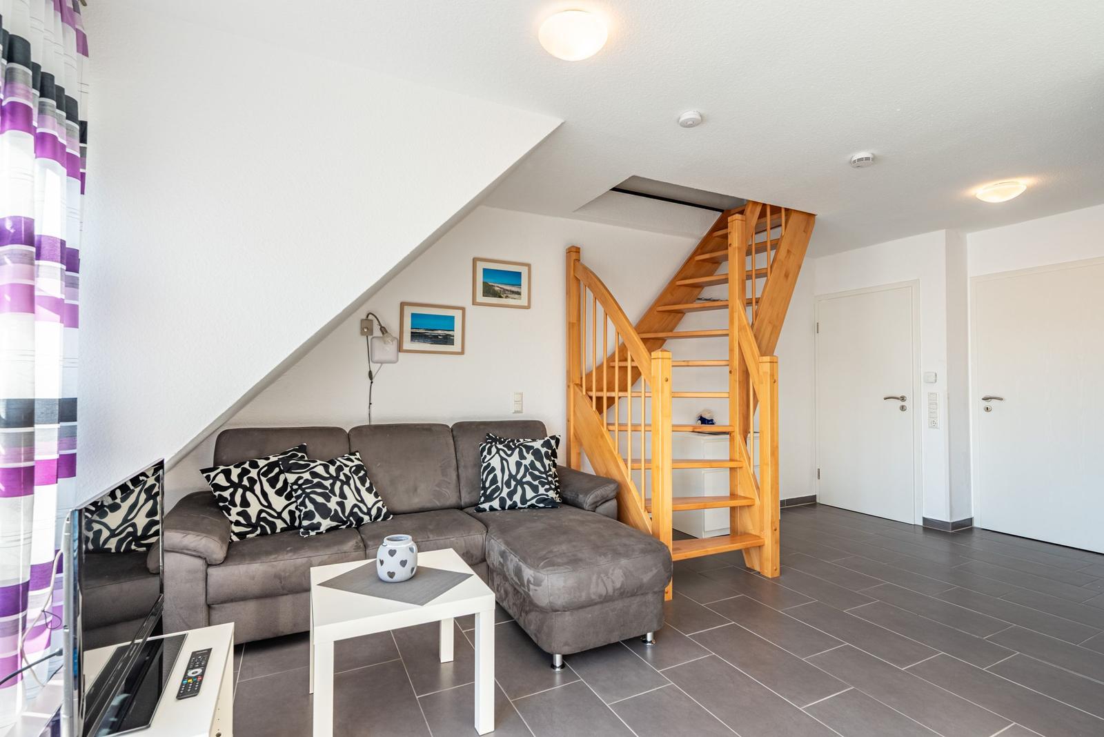 Wohnzimmer mit Sofa, Tisch und Holztreppe zur oberen Etage.