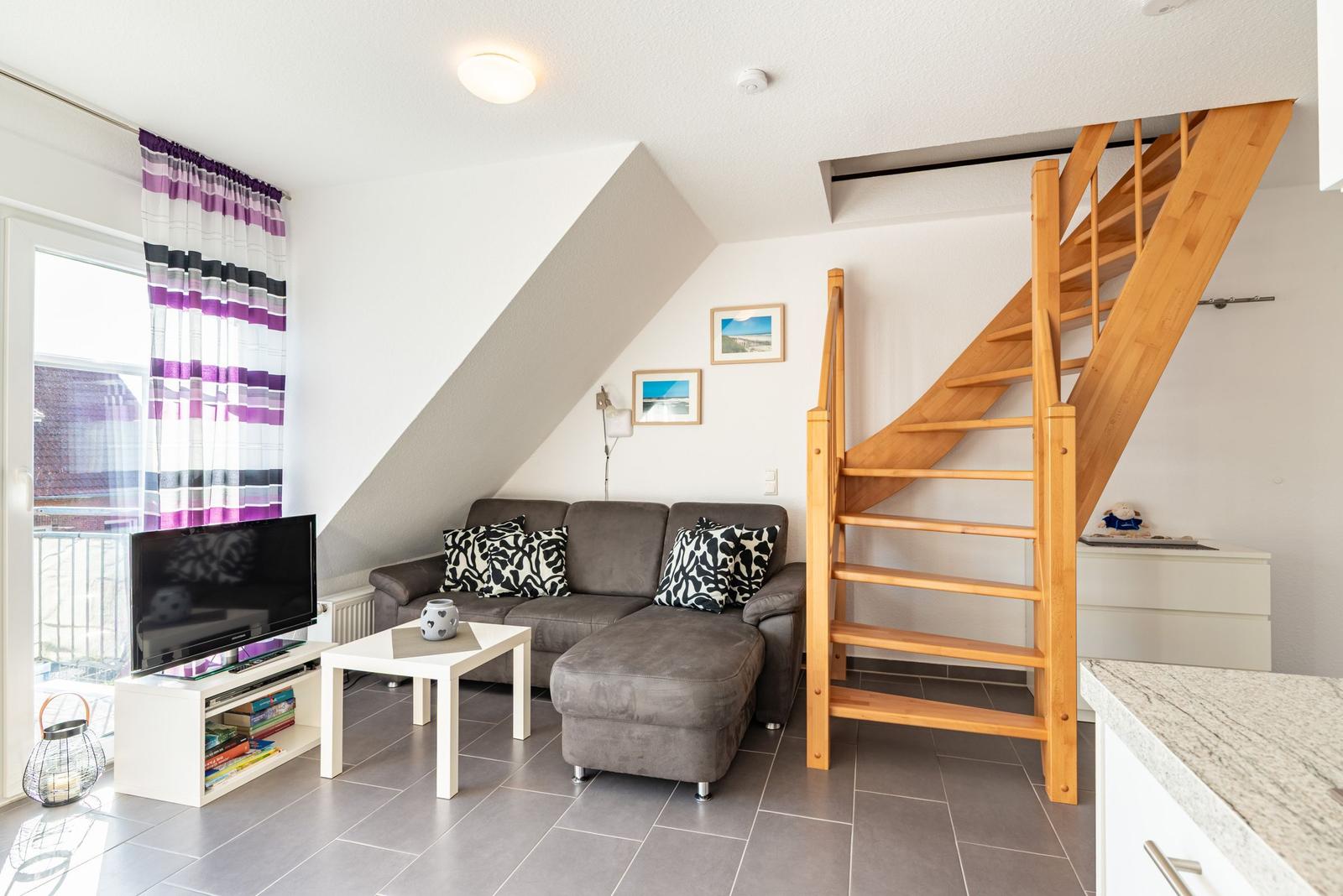 Wohnzimmer mit Sofa, Fernseher und Holztreppe zur oberen Etage.