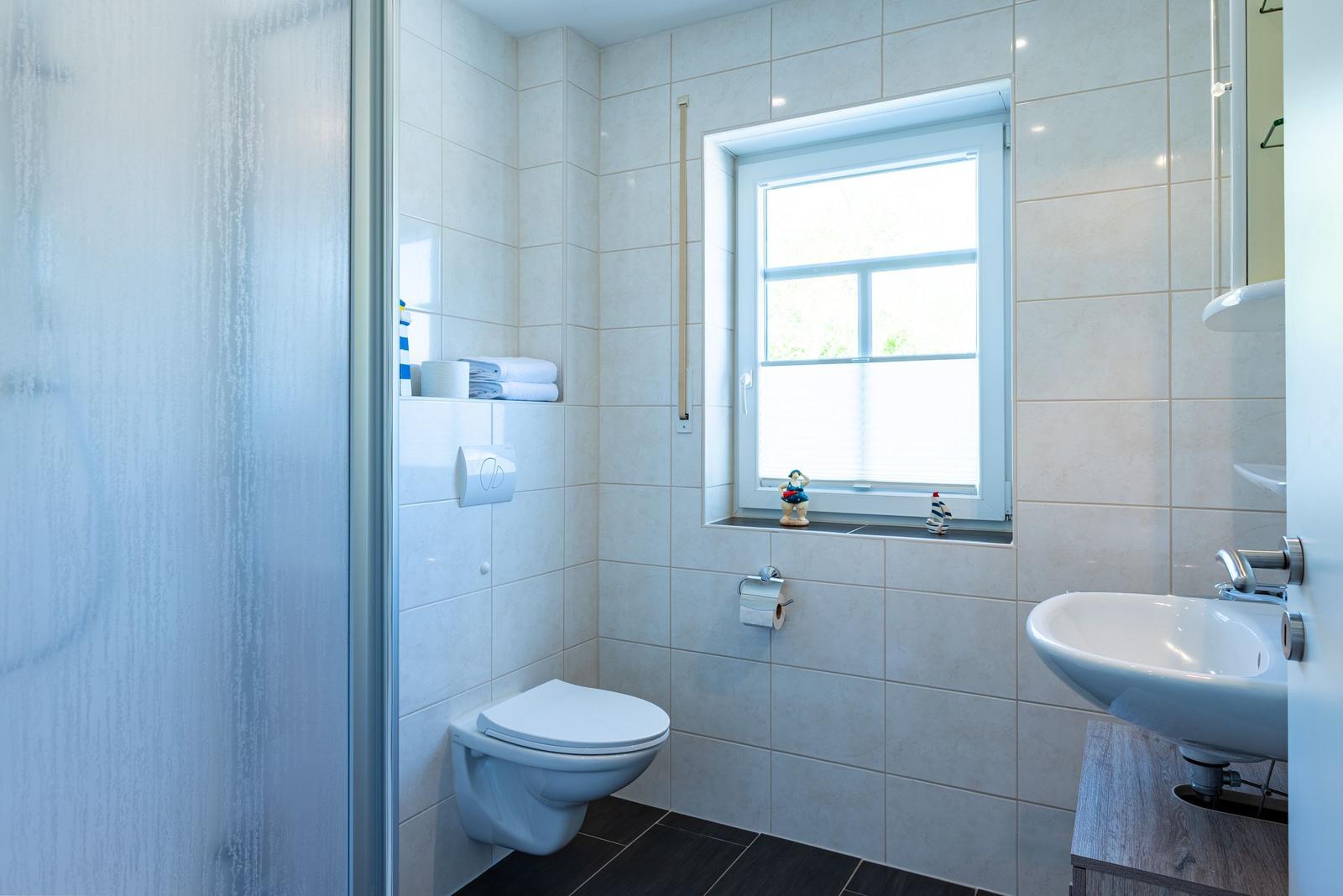 Badezimmer mit Toilette, Waschbecken und Dusche. Fenster mit Blick nach draußen.