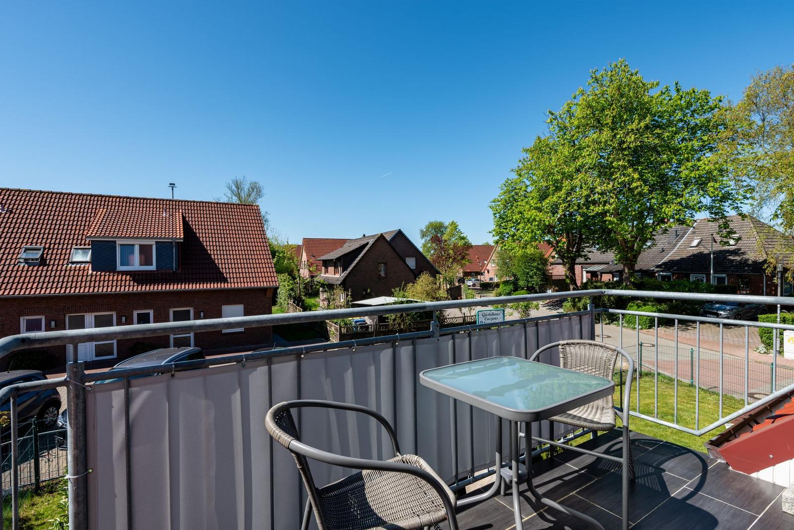 Terrasse mit Tisch und Stühlen. Blick auf Wohnhäuser und Bäume unter blauem Himmel.