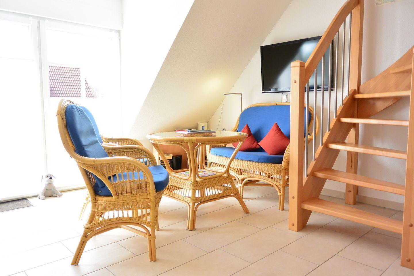 Wohnbereich mit Rattanmöbeln, TV und Treppe zur oberen Etage.