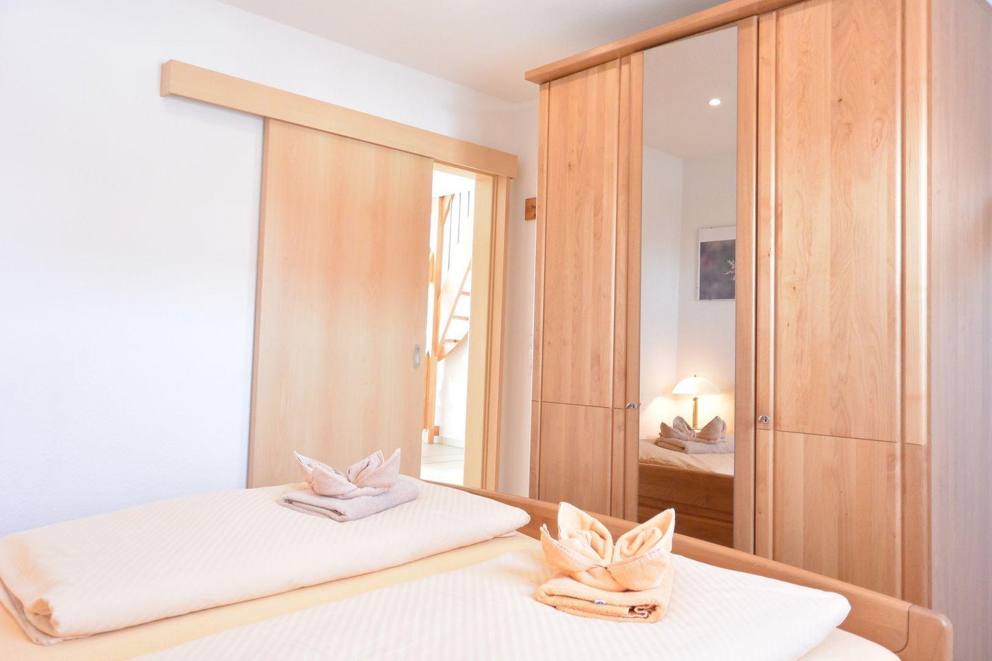 Schlafzimmer mit Bett, Holzschrank und Schlupftür. Handtuch als Vogel dekoriert.