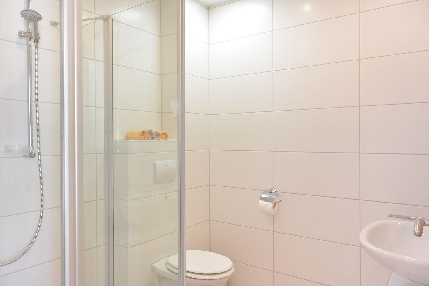 Bad mit Dusche, Toilette und Waschbecken. Handtuch auf Regal.