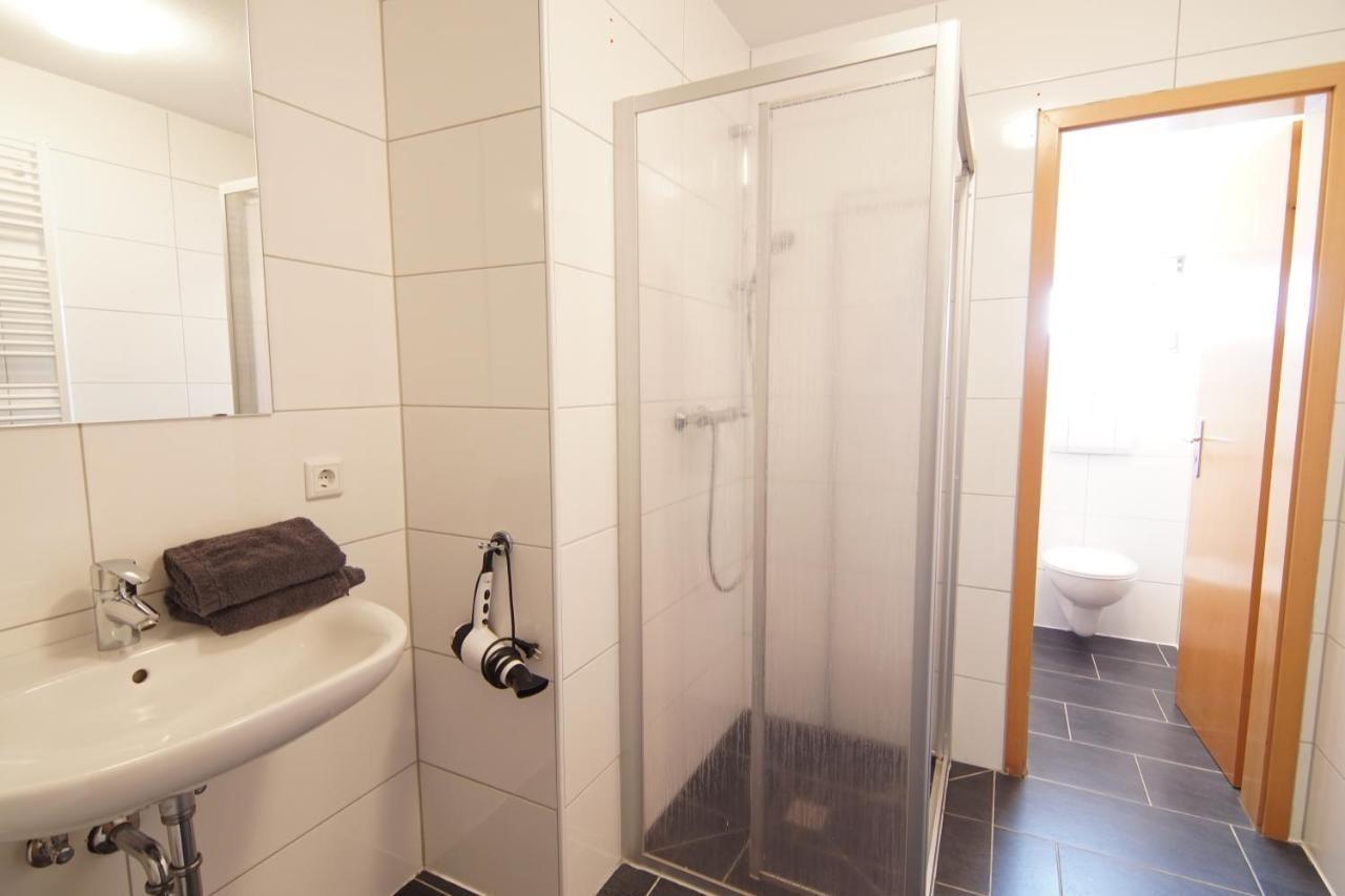 Badezimmer mit Dusche, Waschbecken und Toilette. Fliesenboden und Spiegel.