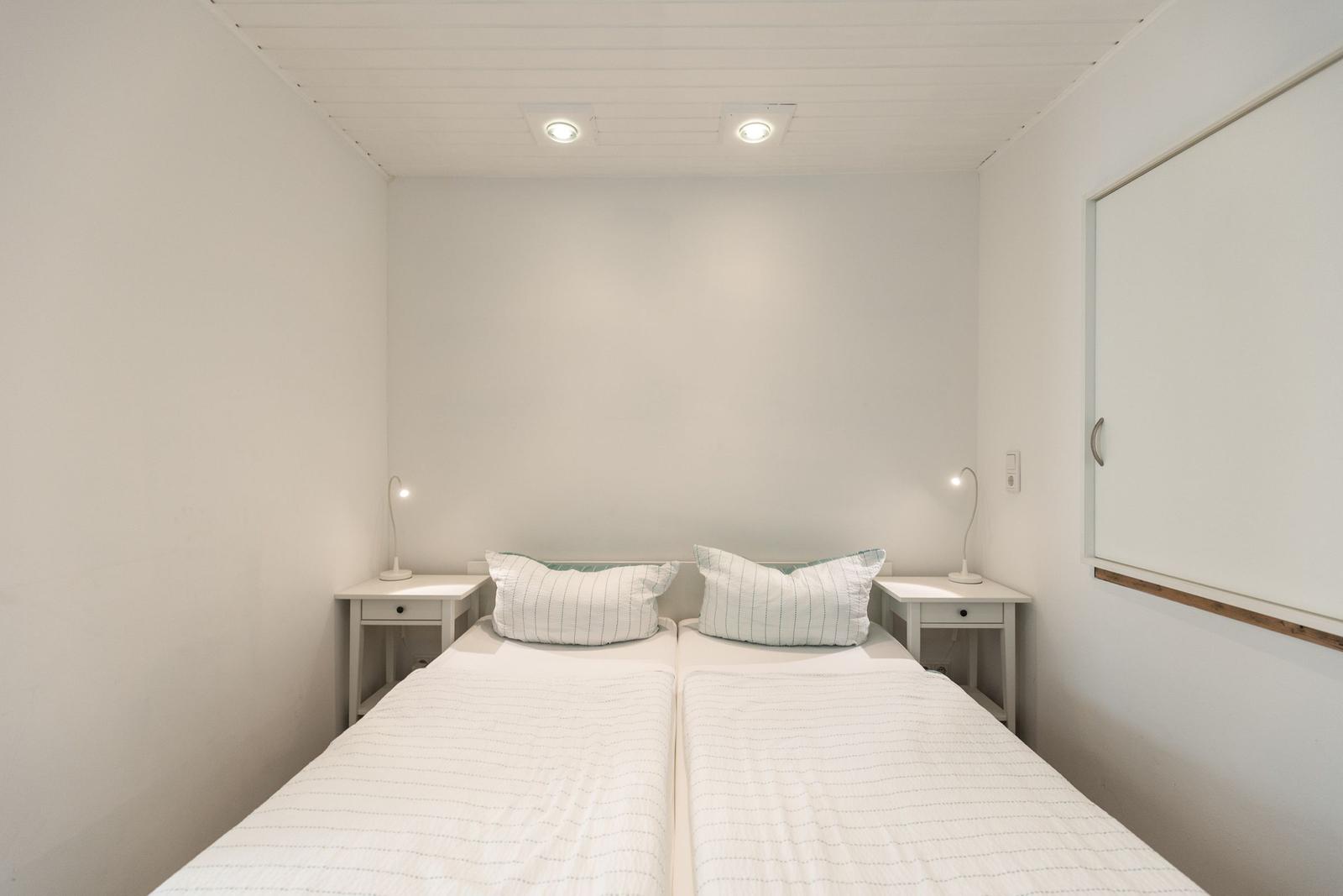 Zimmer mit zwei Betten, Nachttischen und Lampen. Weiße Wände und Decke.