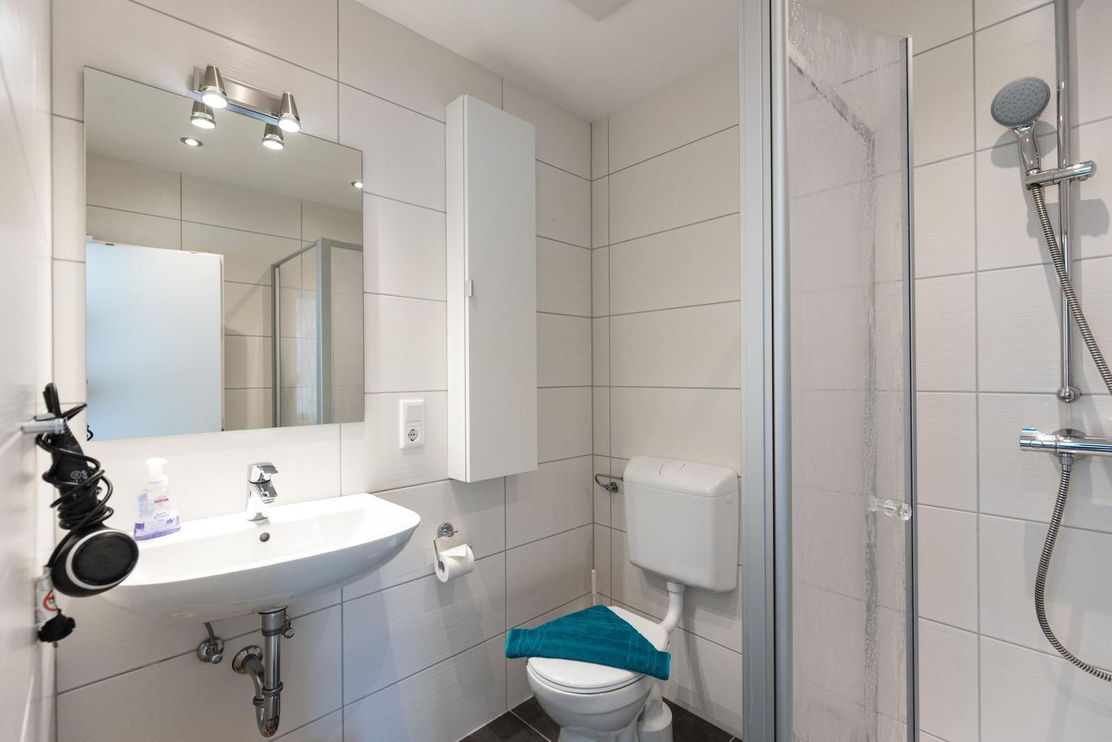 Badezimmer mit Dusche, Toilette und Waschbecken mit Spiegel.