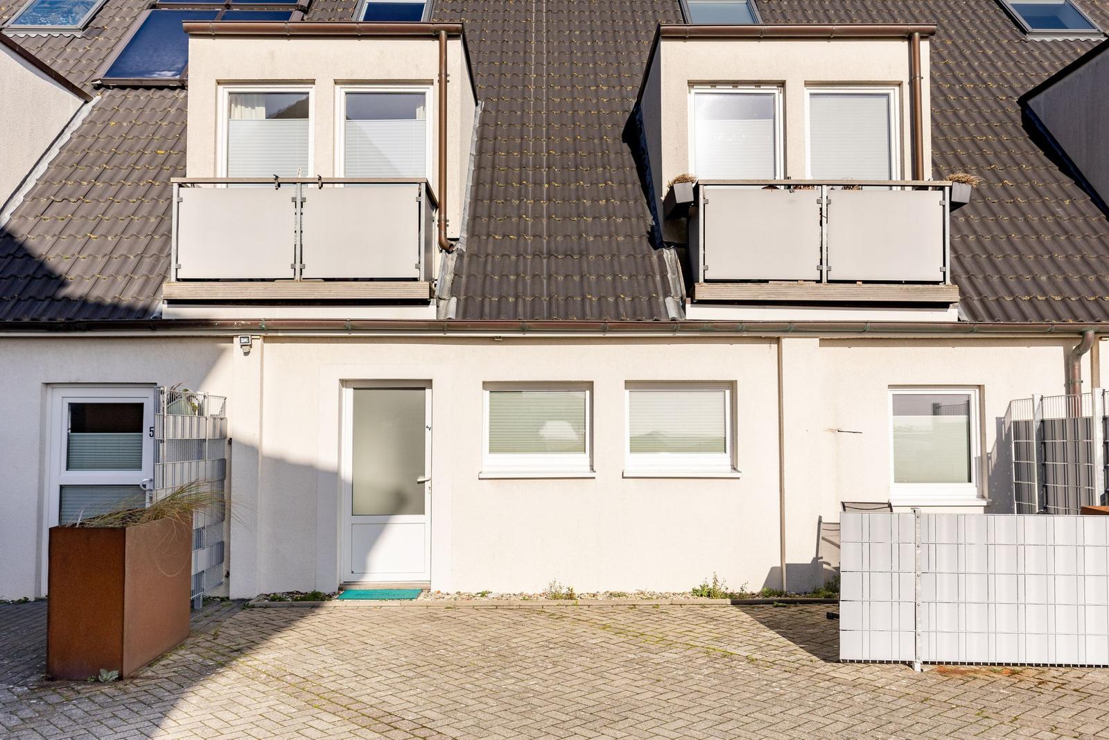Wohnhaus mit Balkonen und Dachfenstern, gepflasterter Vorgarten und weißen Fenstern.