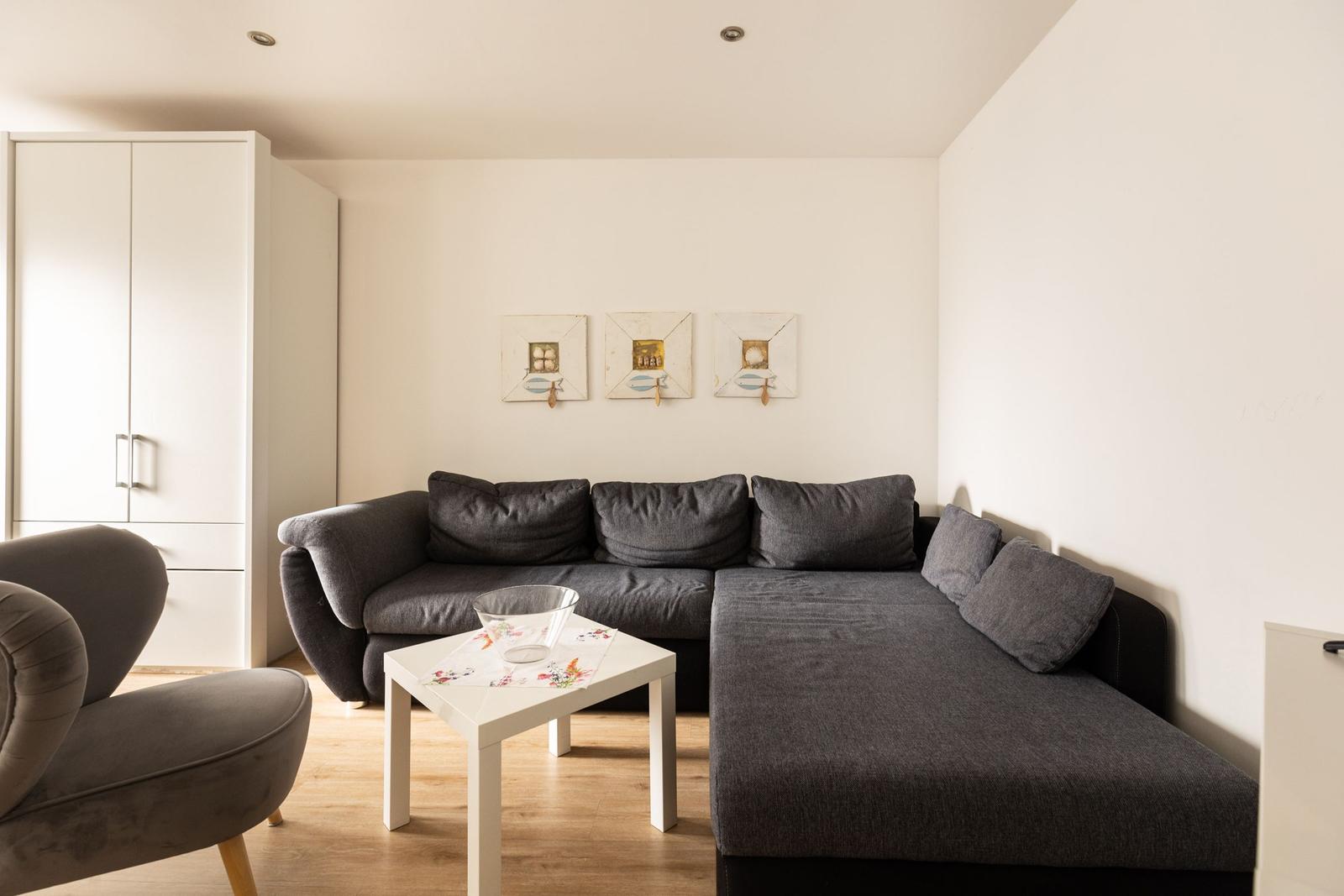 Ein Wohnzimmer mit grauem Sofa, weißem Tisch und weißen Wänden.