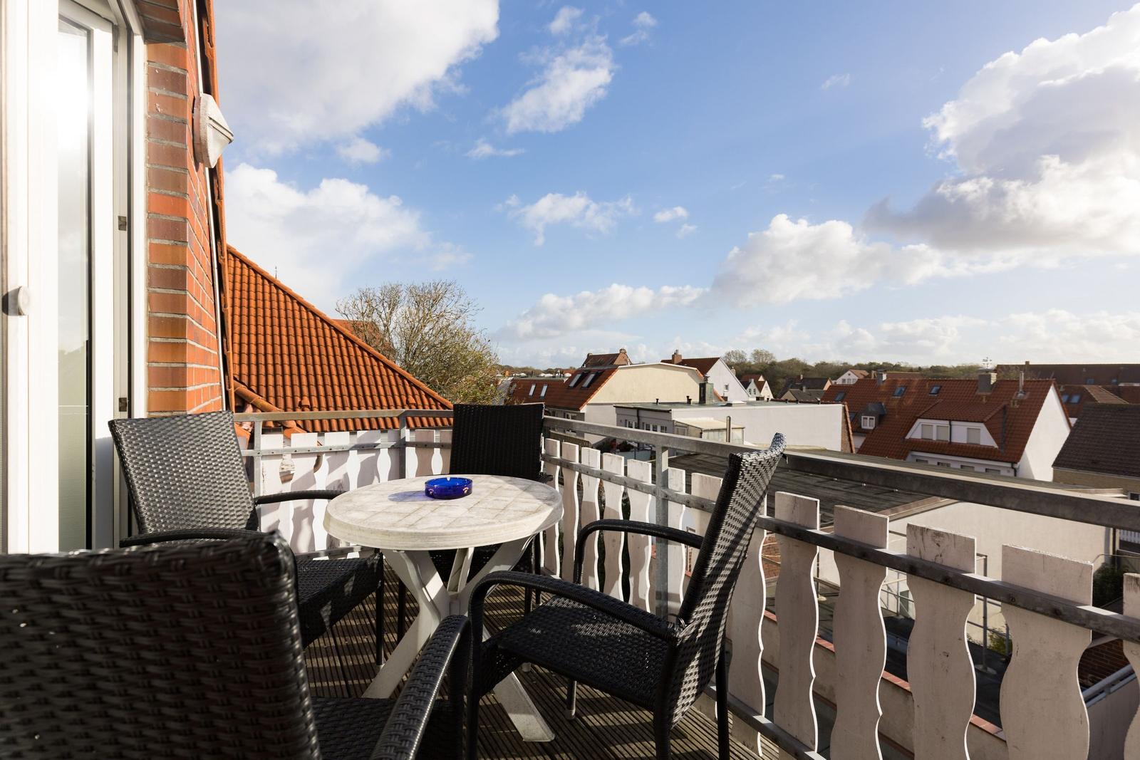 Terrasse mit Tisch und Stühlen, Blick auf Dächer und Himmel.