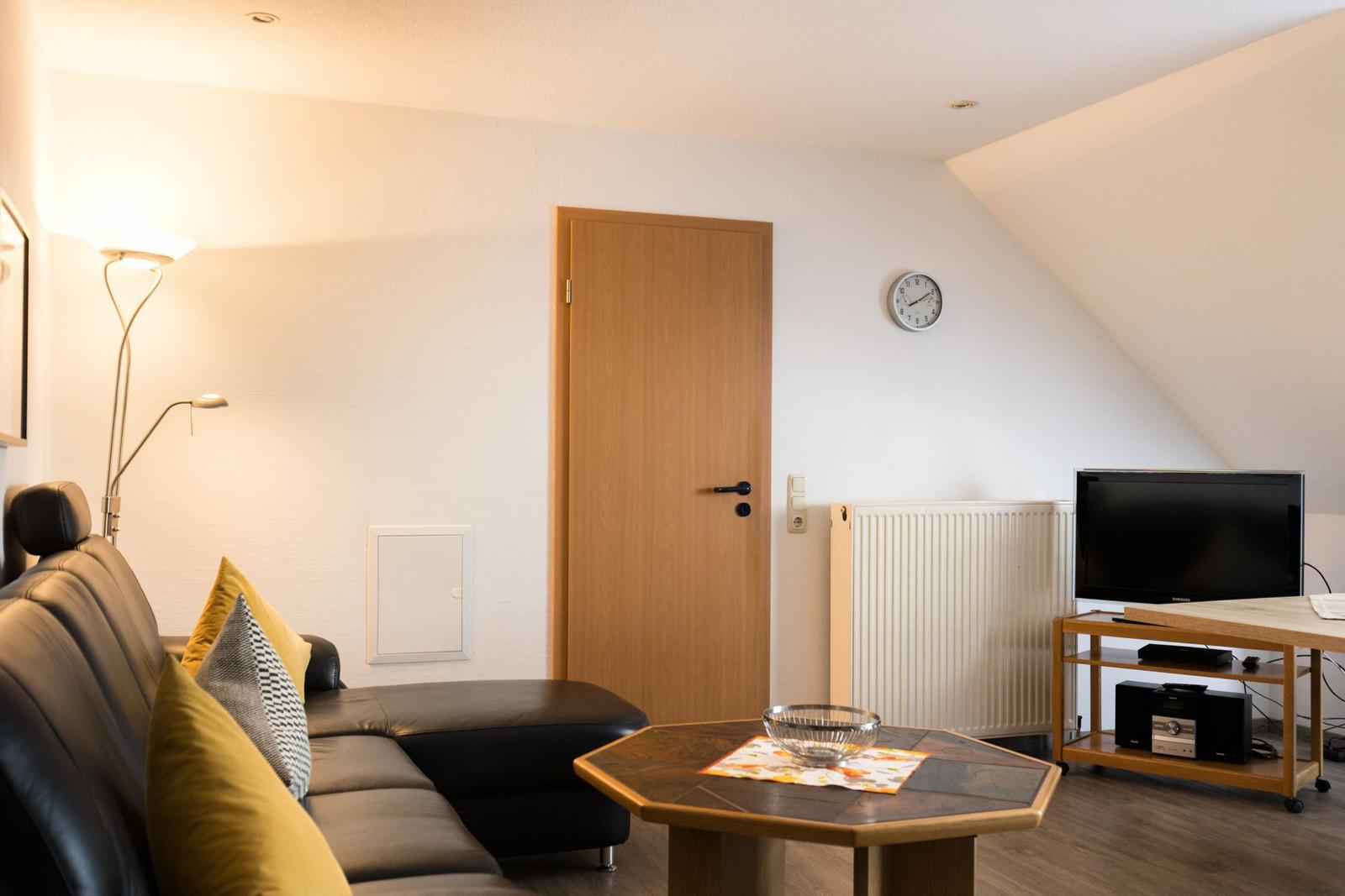 Wohnzimmer mit Sofa, Tisch, Fernseher und Wanduhr.