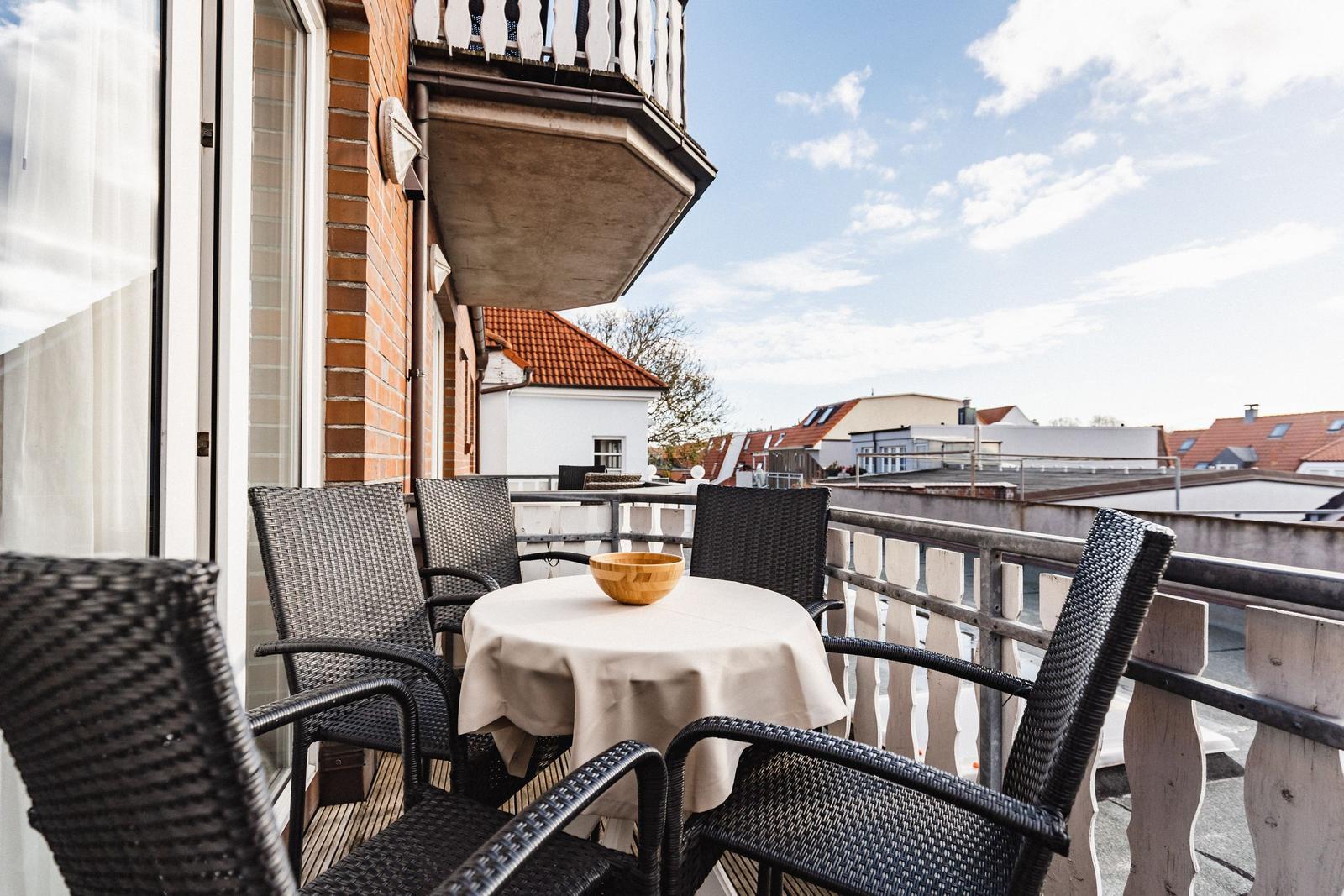 Terrasse mit Tisch und Stühlen, Blick auf Dächer und Himmel.