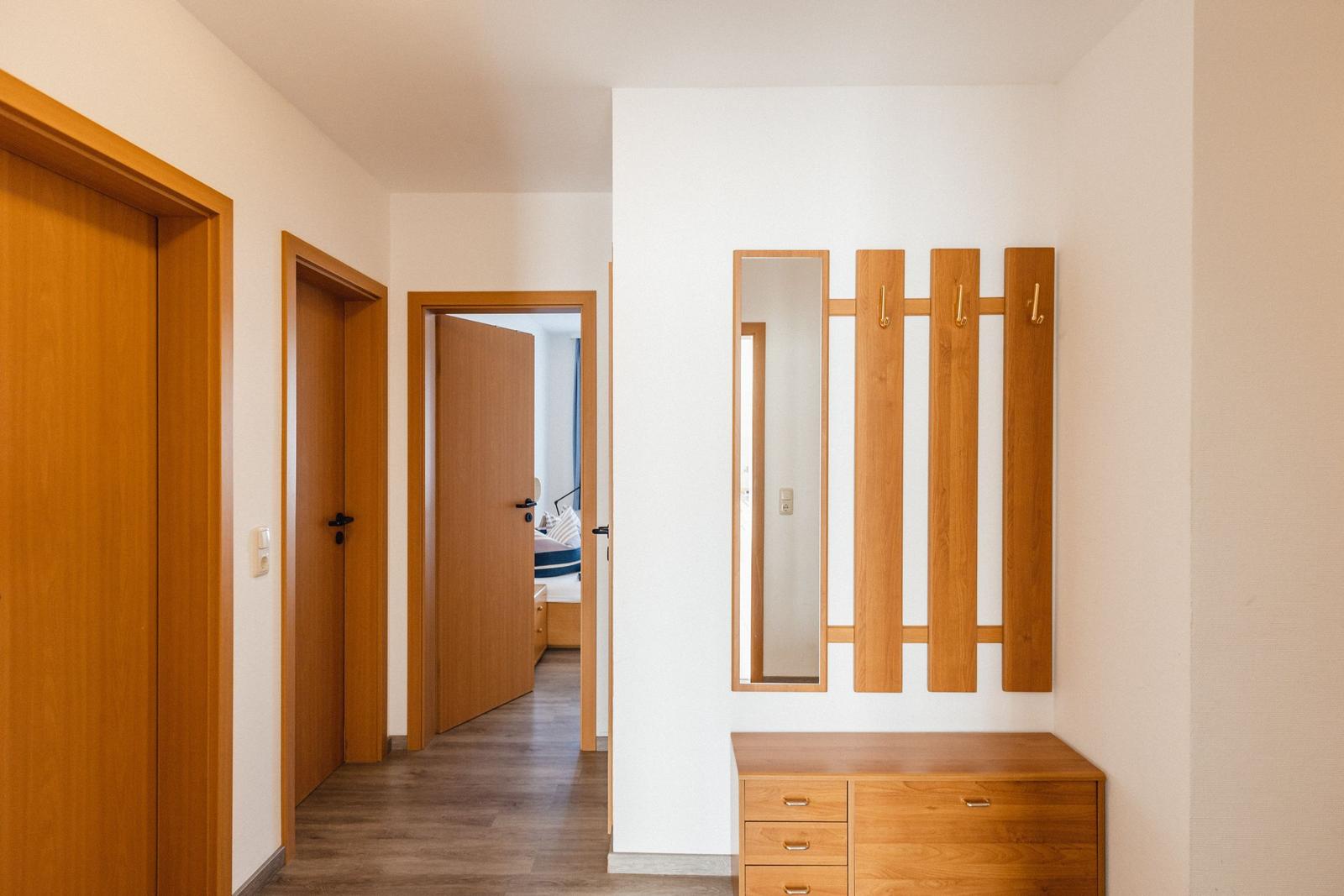 Flur mit Holzmöbeln, Spiegel und Garderobe. Tür zum Schlafzimmer sichtbar.