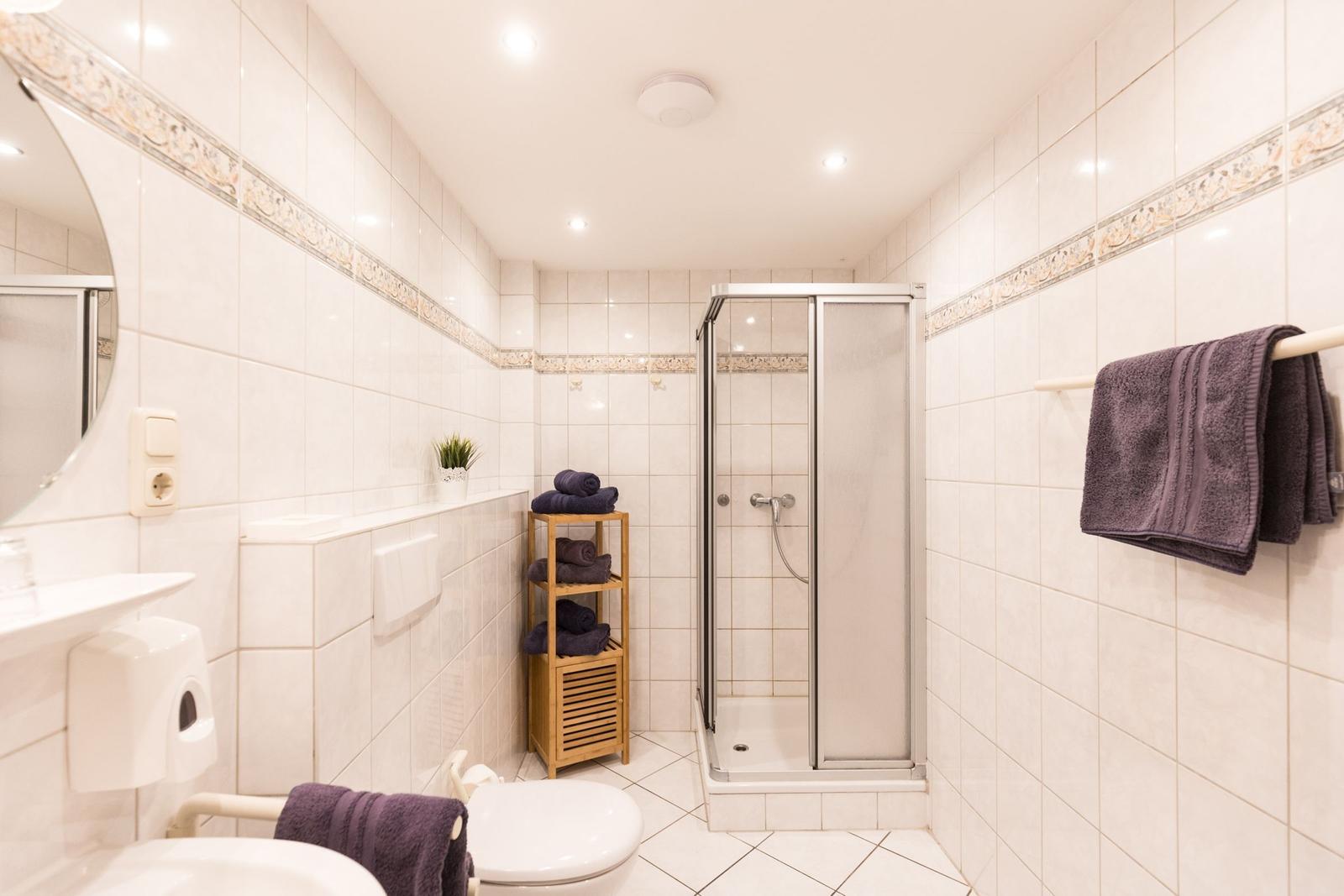 Badezimmer mit Dusche, Toilette und Waschbecken. Wände und Boden sind mit Fliesen verkleidet.
