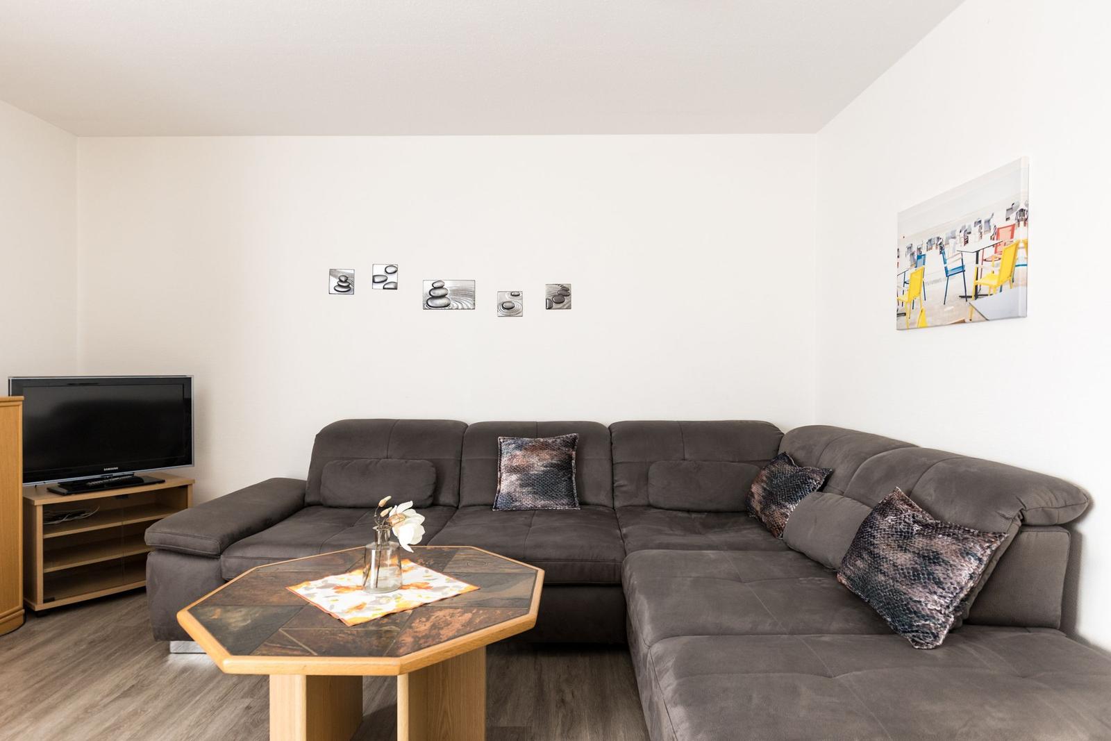 Ein Wohnzimmer mit grauem Sofa, Holztisch und Fernseher an der Wand.