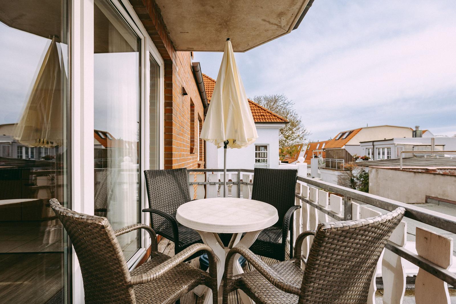 Terrasse mit Tisch, vier Stühlen und geschlossenem Sonnenschirm. Blick auf Dächer und Gebäude.
