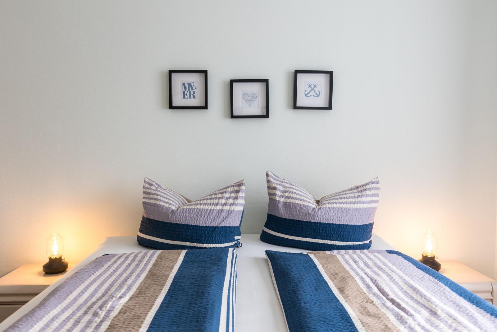 Zwei Betten mit Streifenbetten und Kissen, Wand mit drei Bildern und Nachttischlampen.