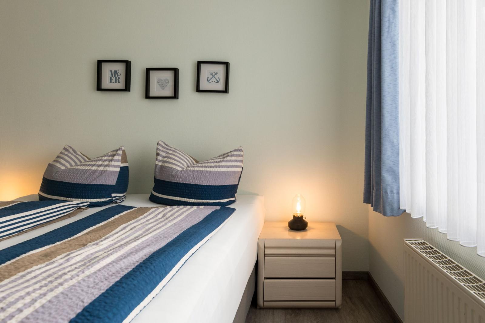 Schlafzimmer mit Bett, Nachttisch und Fenster mit Vorhängen.