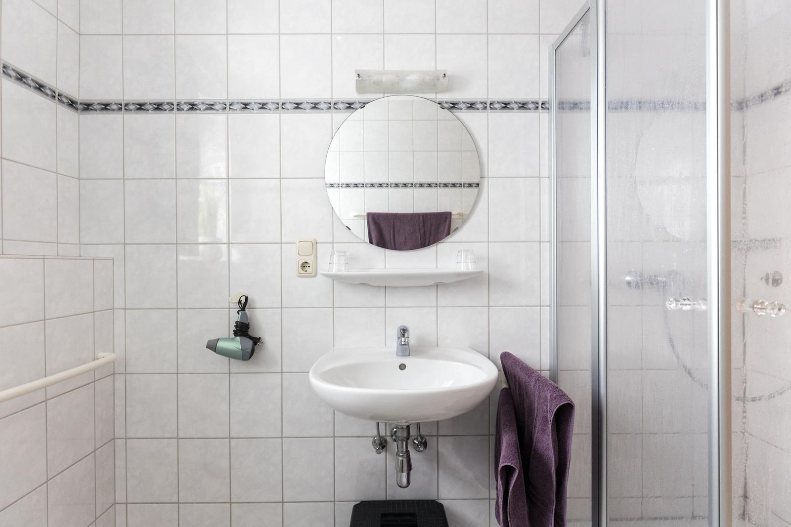 Badezimmer mit Dusche, Waschbecken und runden Spiegel