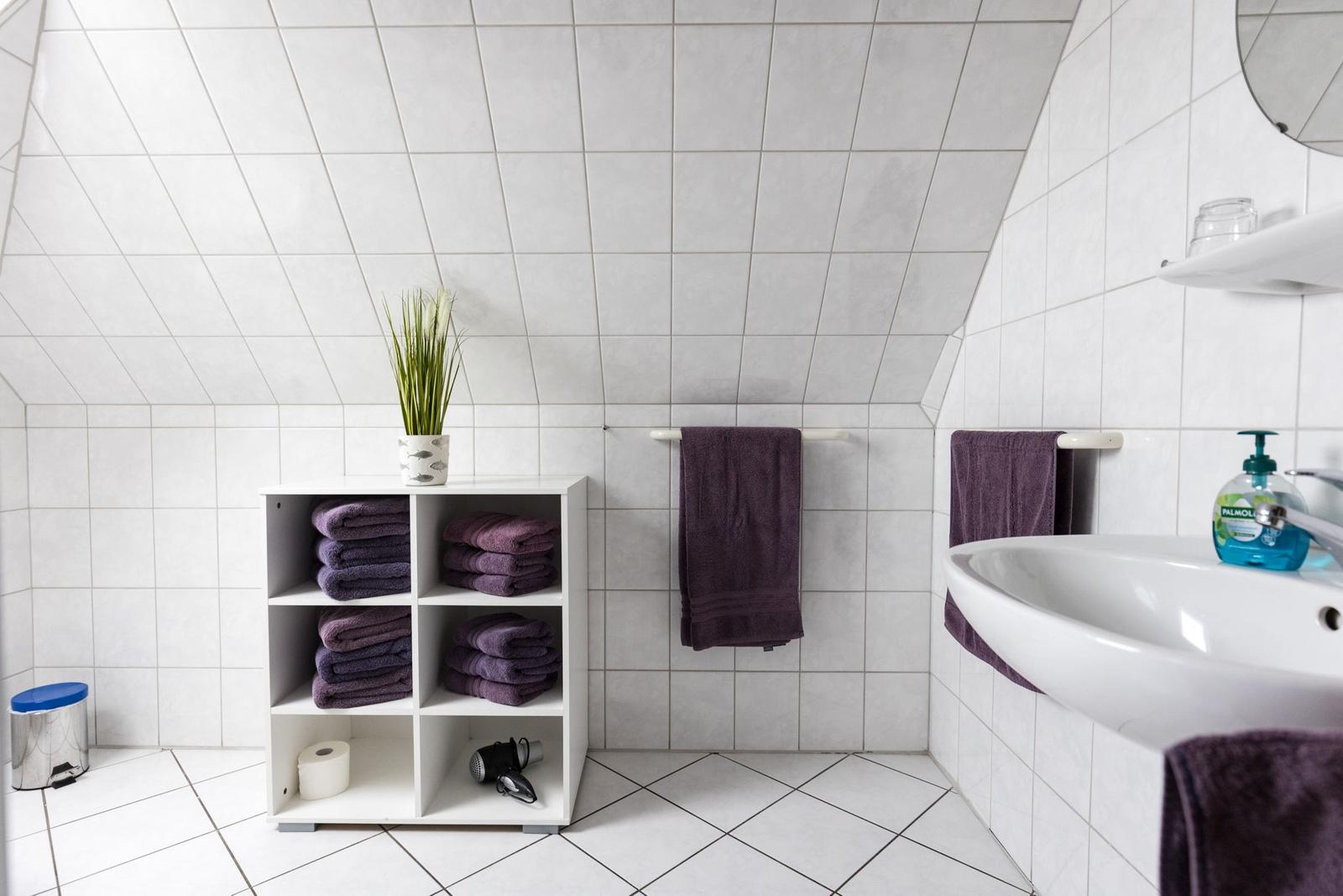 Badezimmer mit weißen Fliesen, Handtuchhalter und Regal mit Handtüchern.