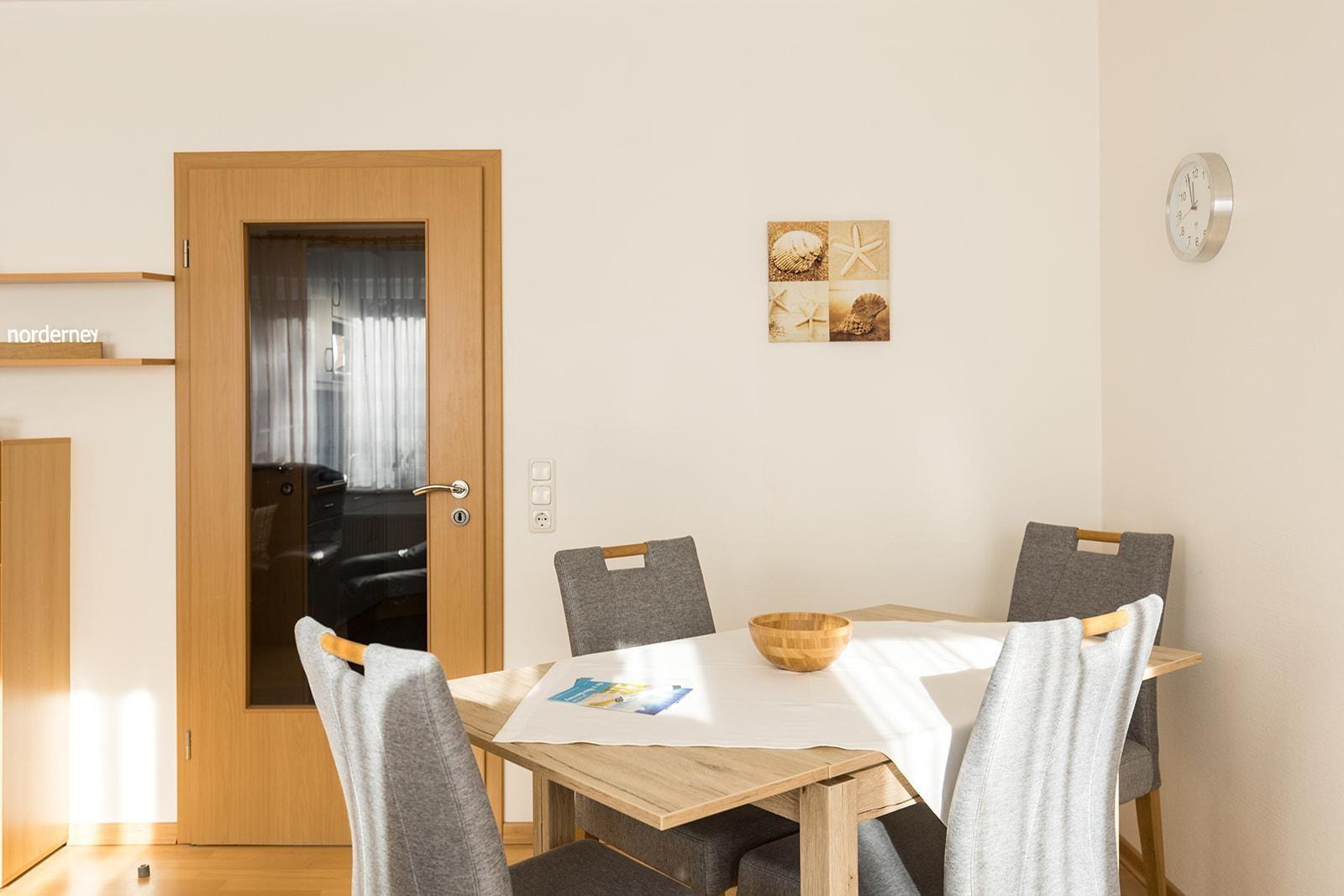 Esszimmer mit Tisch, Stühlen und Wandbildern. Tür führt in Wohnbereich.