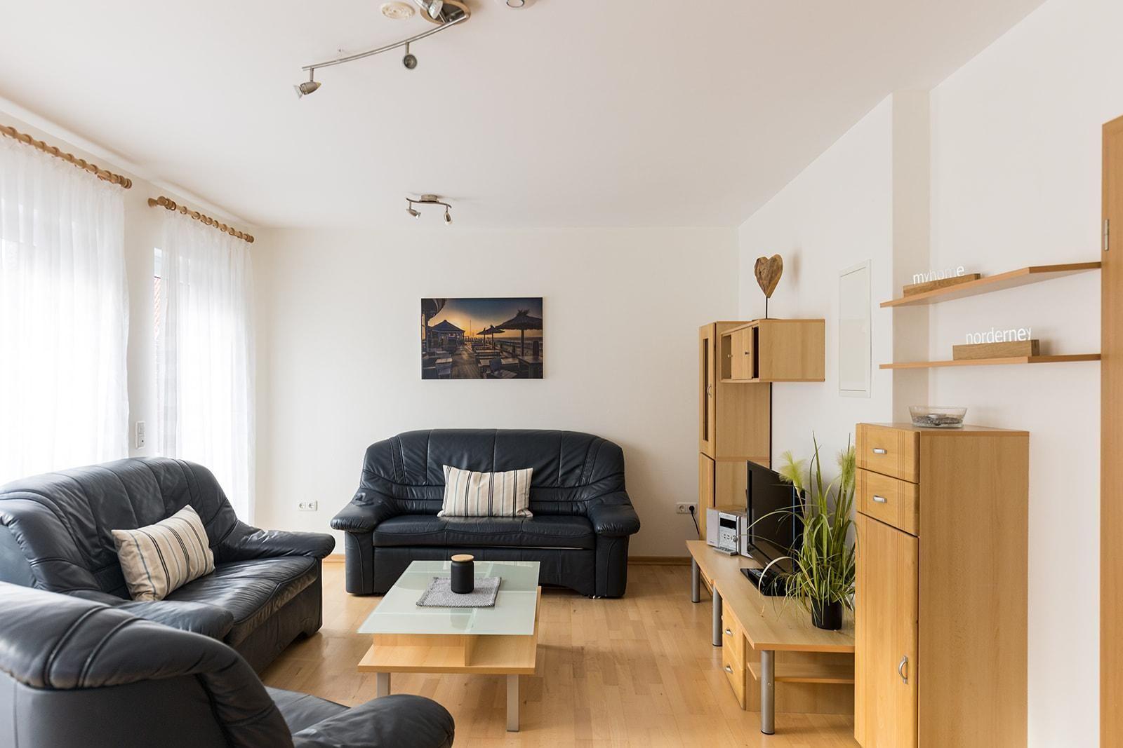 Wohnzimmer mit zwei schwarzen Ledersofas, Glas-Tisch und Holzmöbeln.