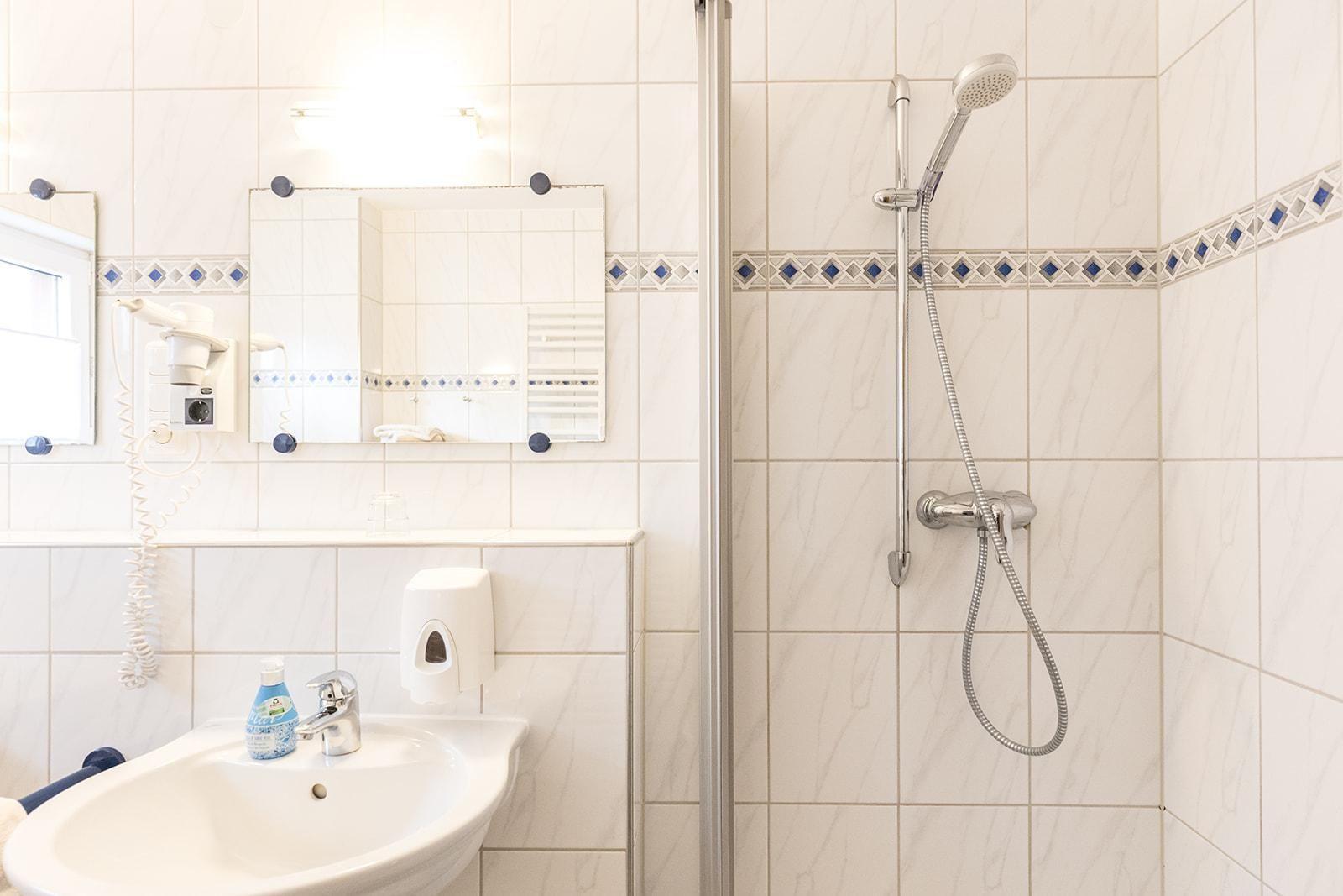 Badezimmer mit Dusche, Waschbecken und Spiegel an der Wand.
