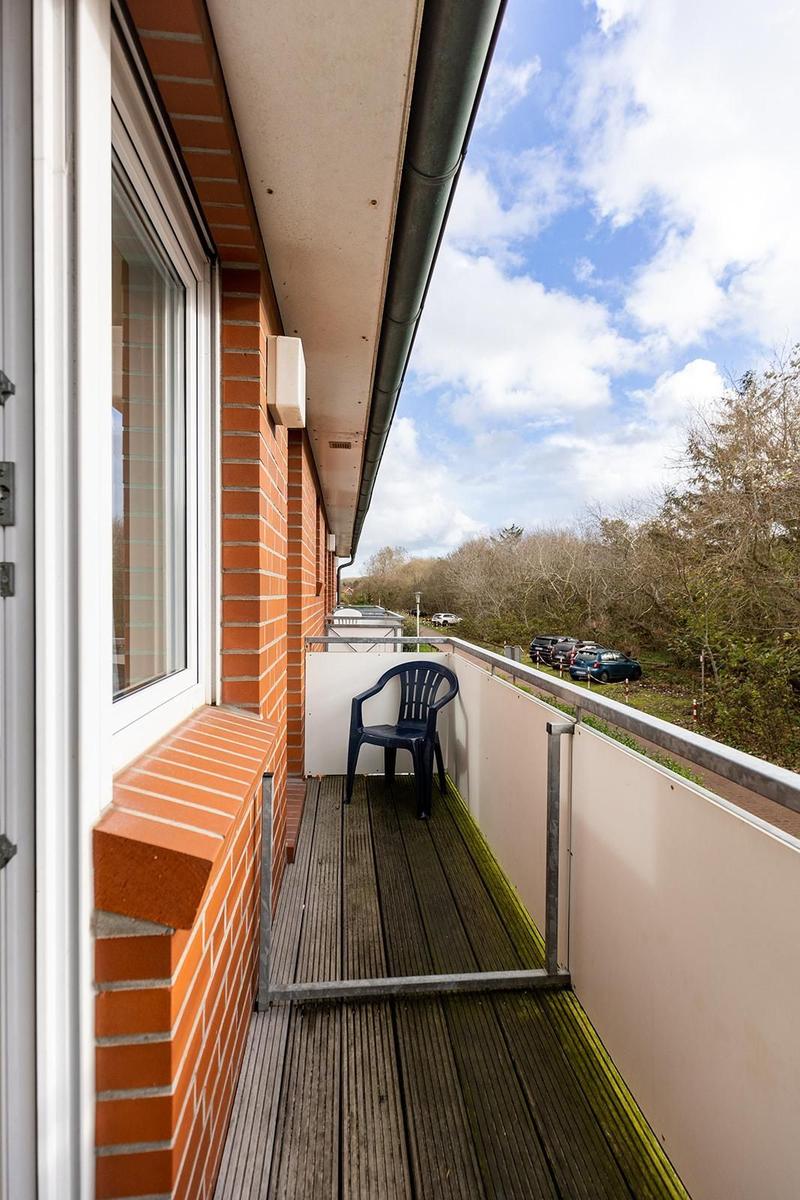 Balcony with wooden floor, blue plastic chair, and view of trees and parked cars.