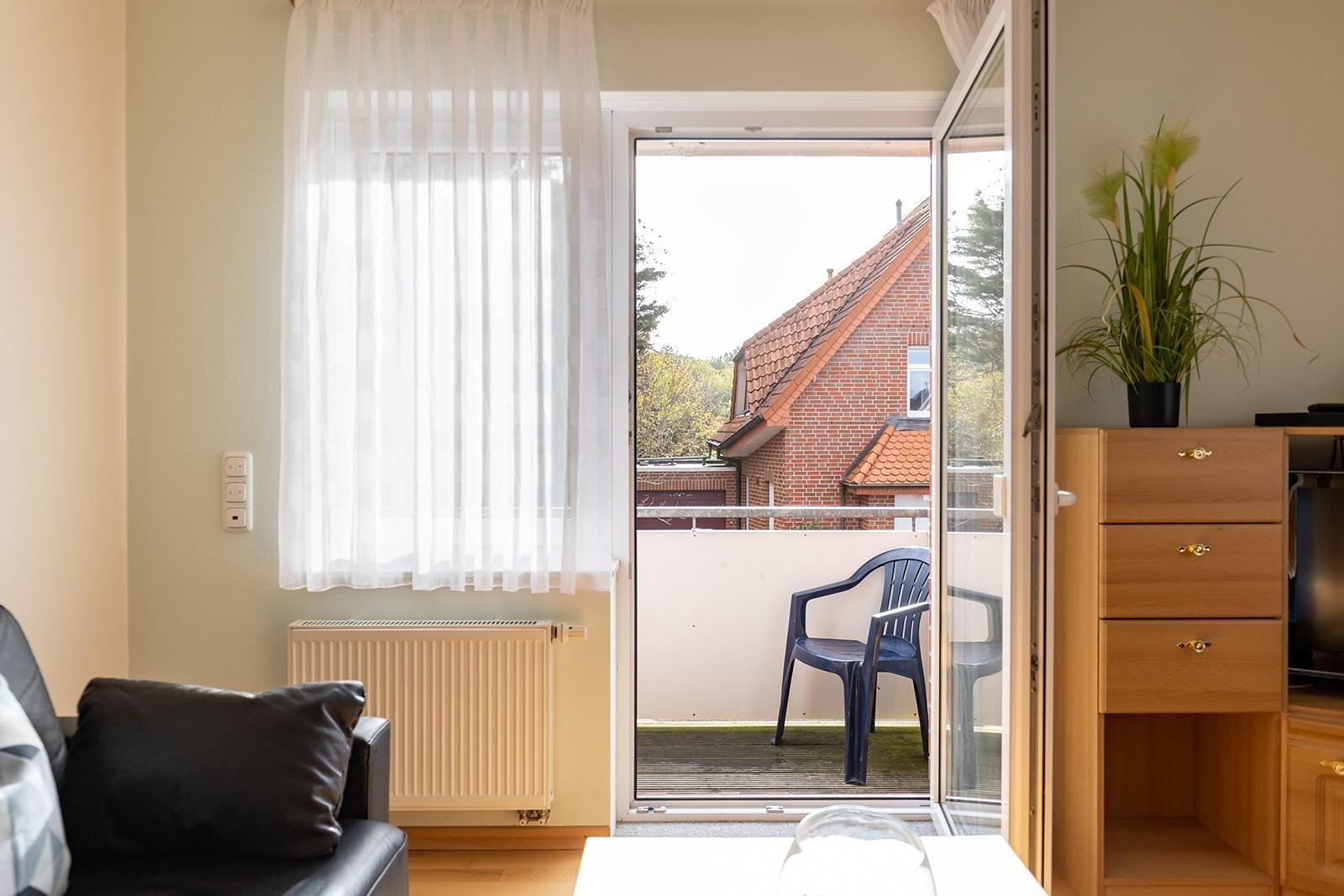 Durch die Glastür gelangt man auf die Terrasse mit Stuhl. Im Raum steht ein Sofa und ein Schrank.