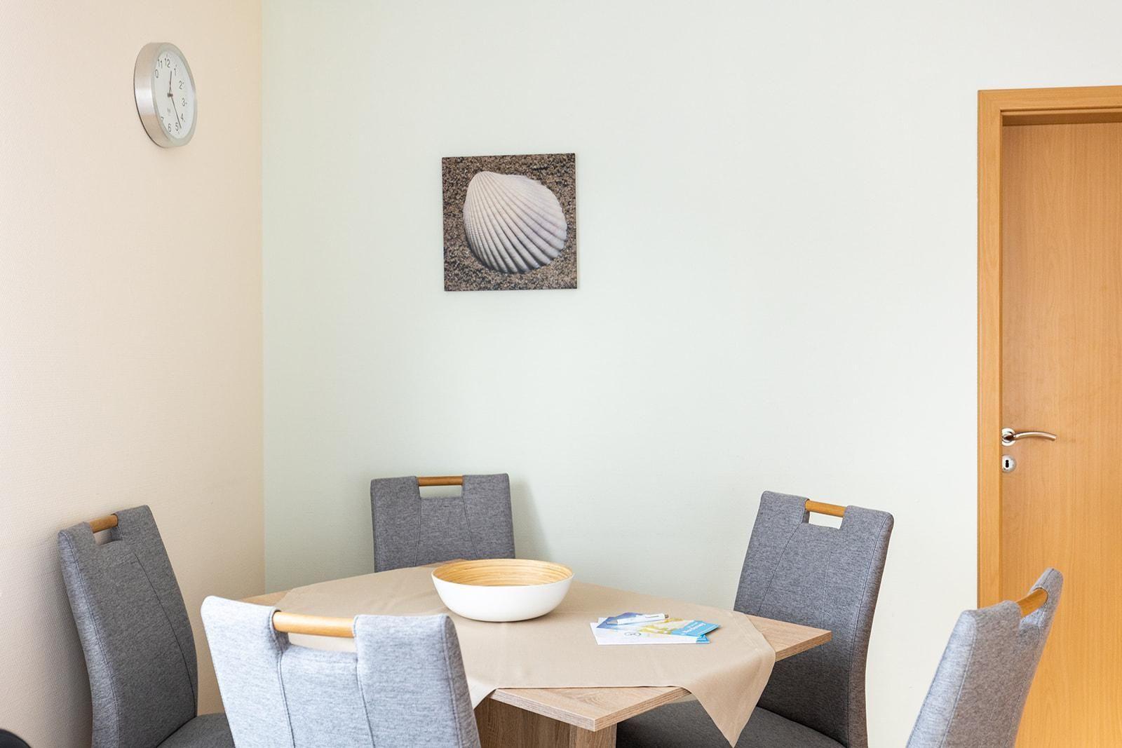 Esszimmer mit runder Tisch, vier Stühlen, Wanduhr und Bild einer Muschel.