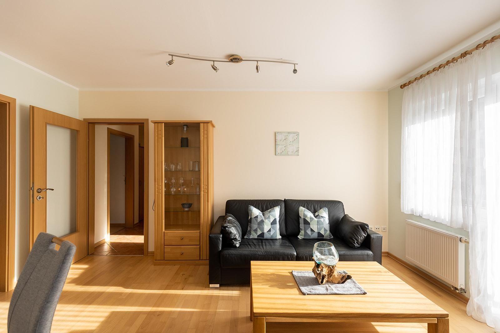 Wohnzimmer mit schwarzer Couch, Holztisch und Glasvitrine.