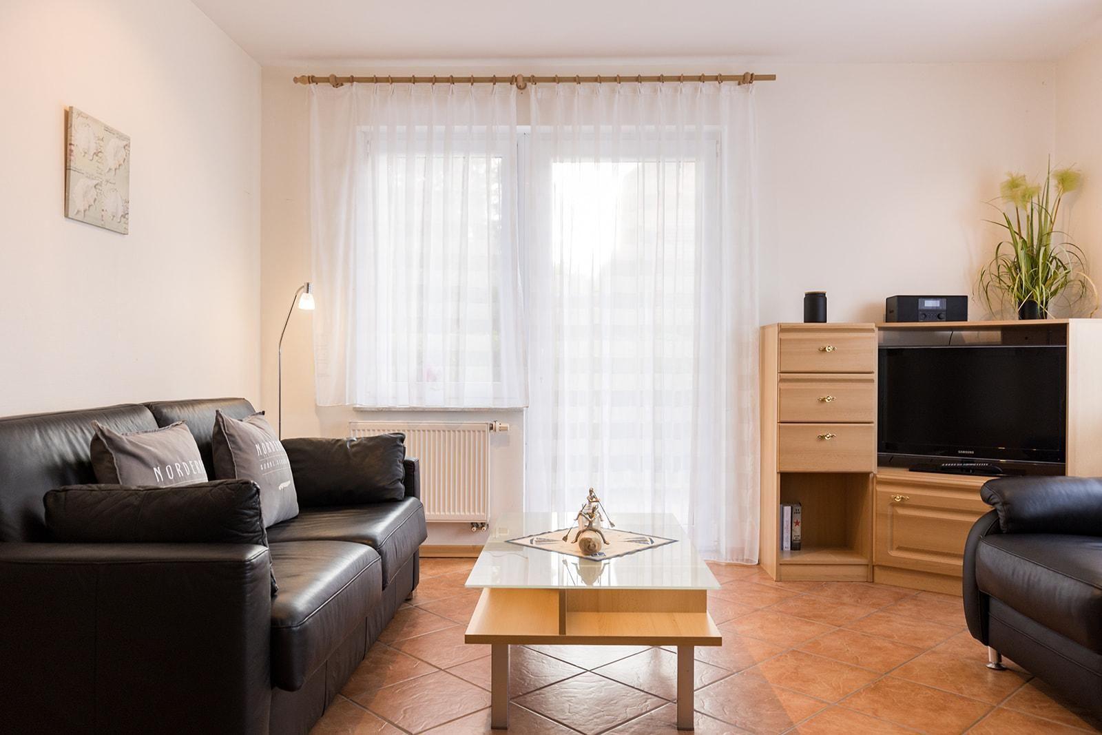 Living room with leather sofa, glass table, and TV on wood cabinet.
