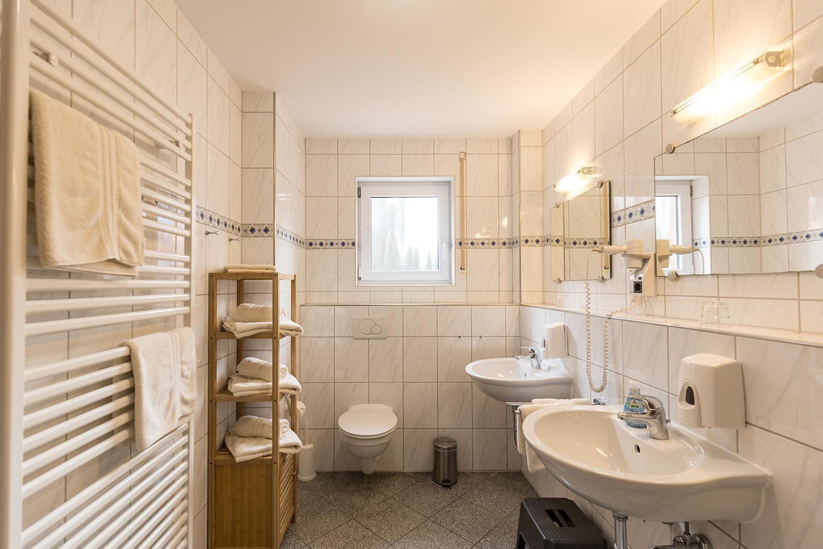 Bathroom with shower, sink, and toilet. White tiles and towel rack.