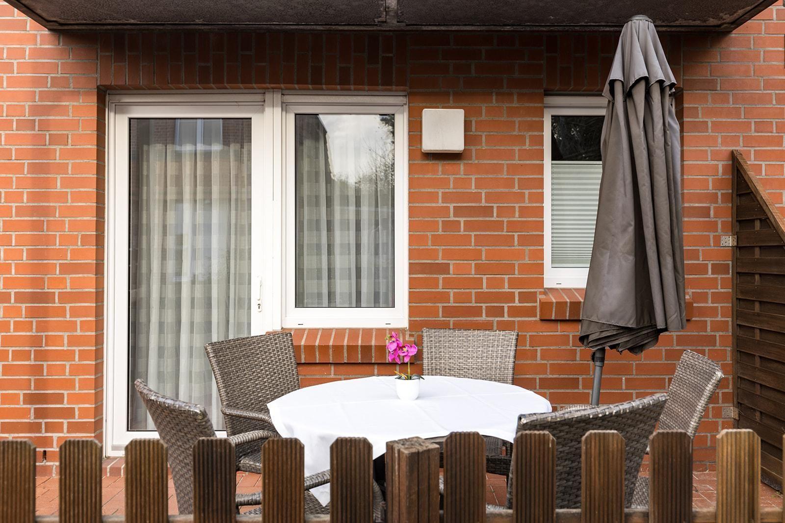 Terrace with round table, four chairs, and closed umbrella against brick wall.