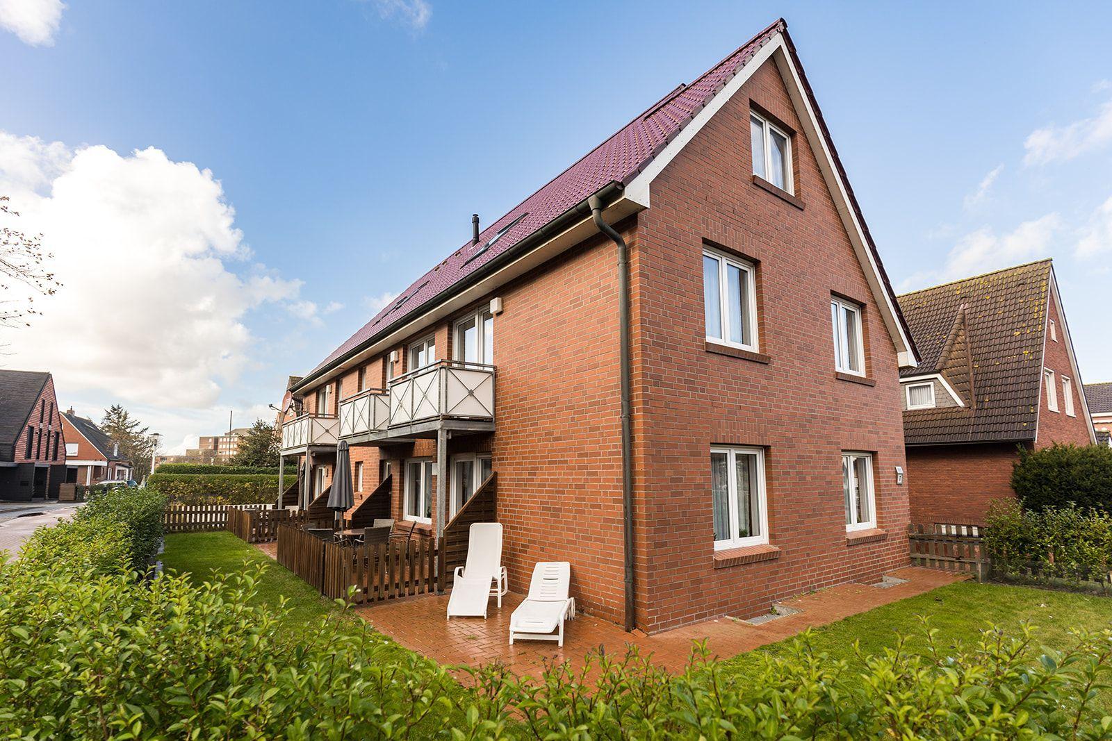 Two-story house with balcony, terrace, and garden area. White sun loungers are available.