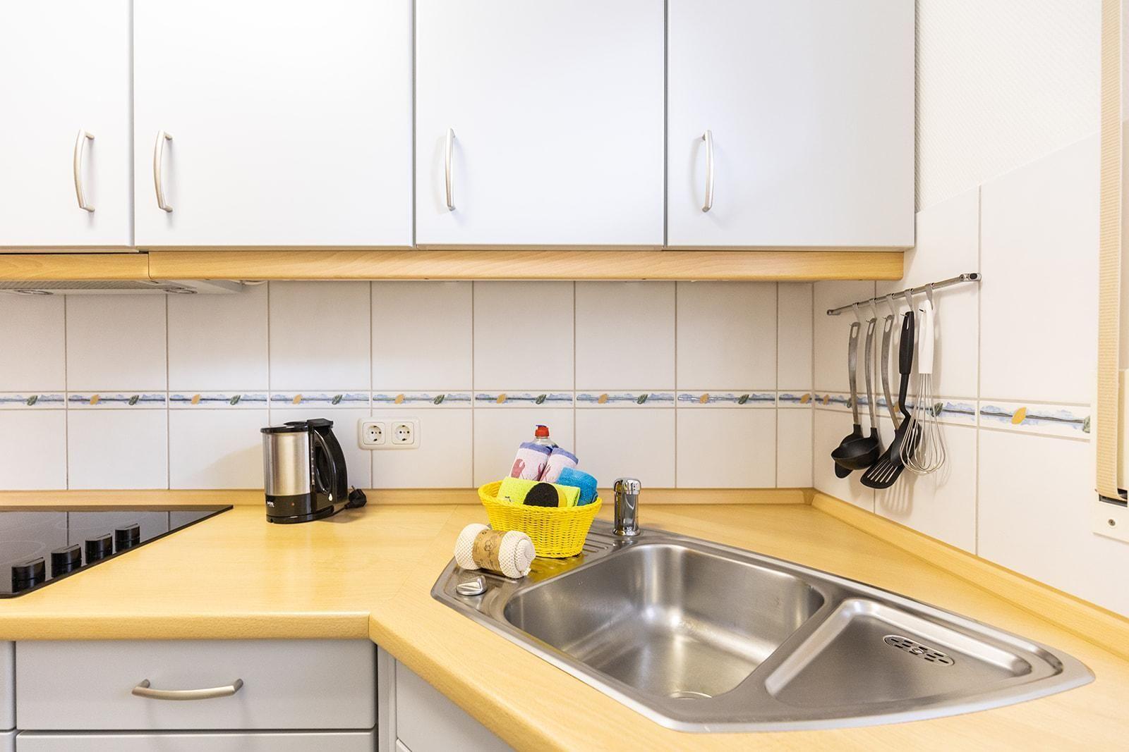 Kitchen with stainless steel sink, wooden countertop, and white cabinets.