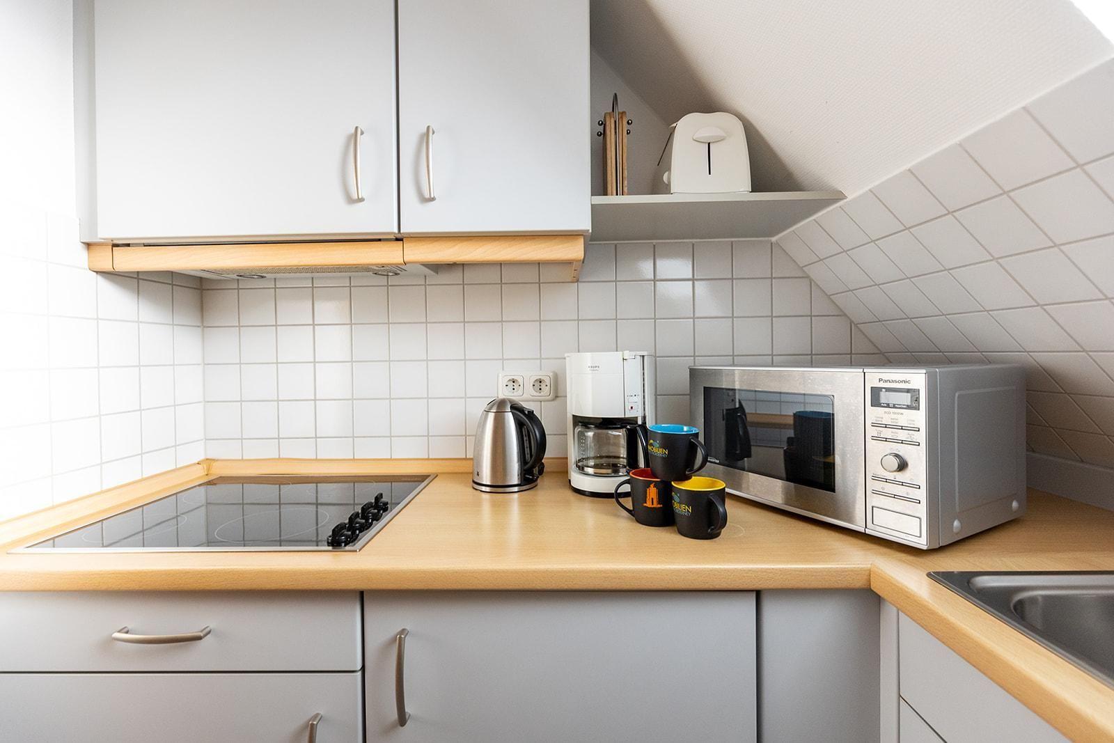 Küche mit Kochfeld, Mikrowelle, Kaffeemaschine und Kaffeetassen.