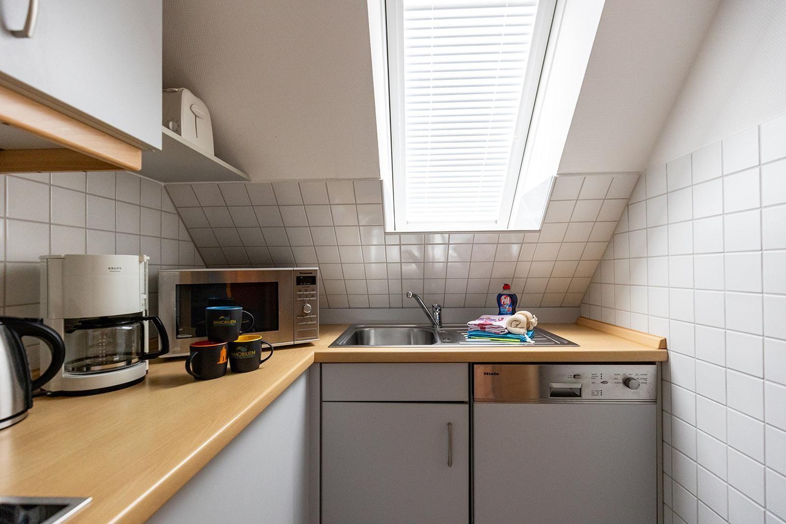 Küche mit Spüle, Mikrowelle, Kaffeemaschine und Waschmaschine unter Dachschrägen.