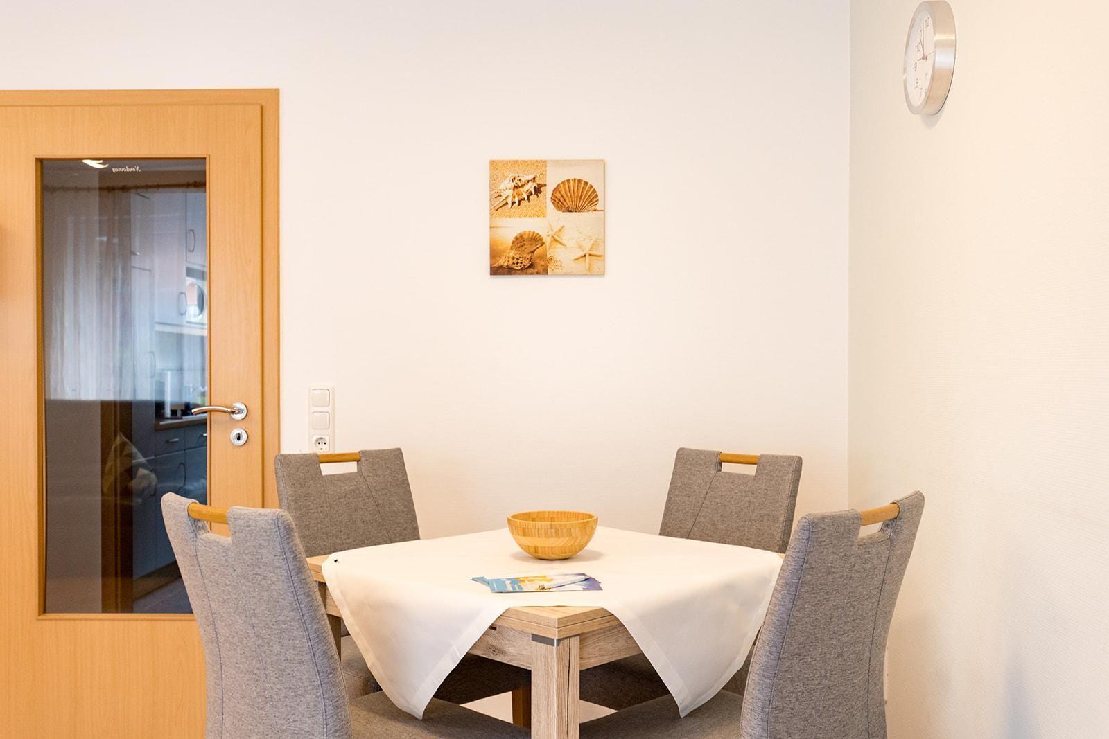 Esszimmer mit Tisch, vier Stühlen und Wandbild mit Muscheln.