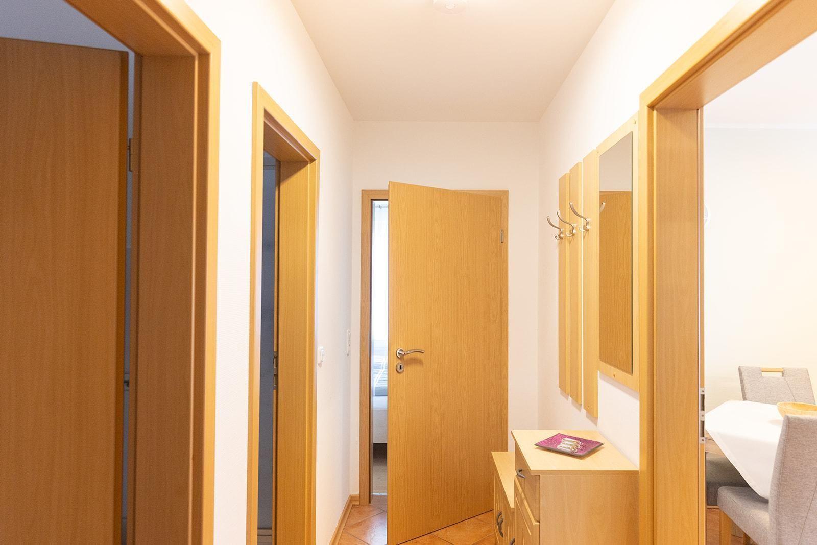 Flur mit Holztüren und Kleiderhaken an der Wand. Blick in Schlafzimmer und Essbereich.