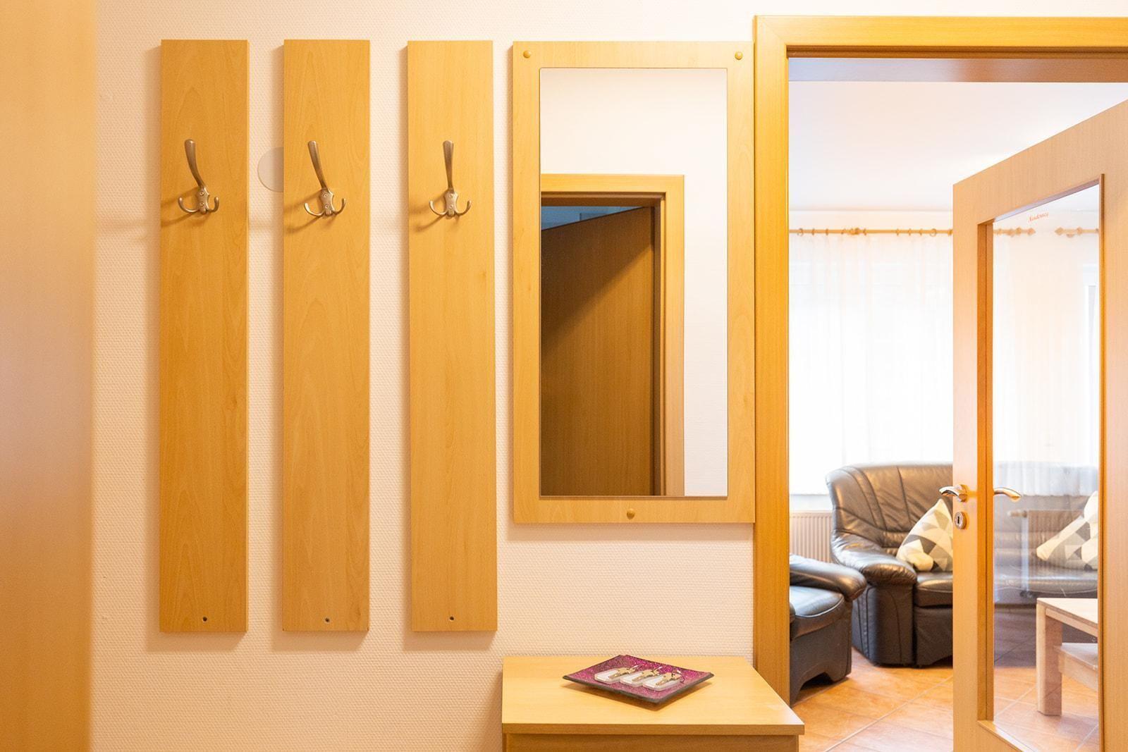 Eingangsbereich mit Holzgarderoben und Spiegel. Durchgang zu Wohnzimmer mit Ledersofa.