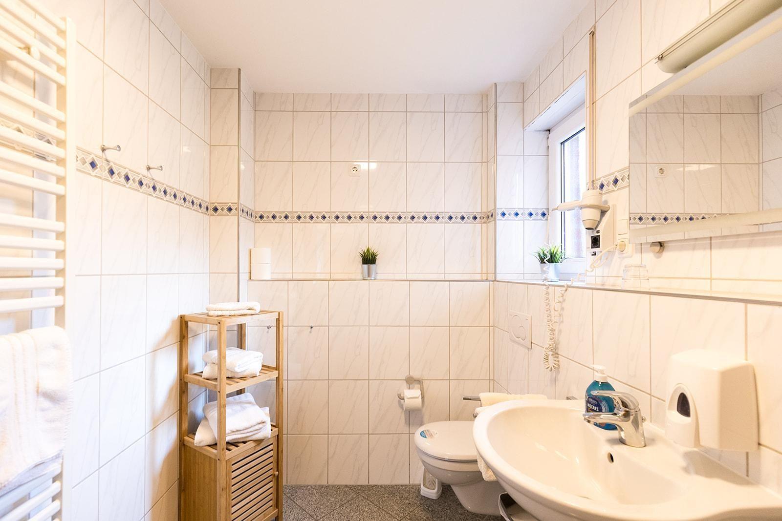 Badezimmer mit Toilette, Waschbecken und Handtuchständer. Fliesenwand mit blauer Zierleiste.