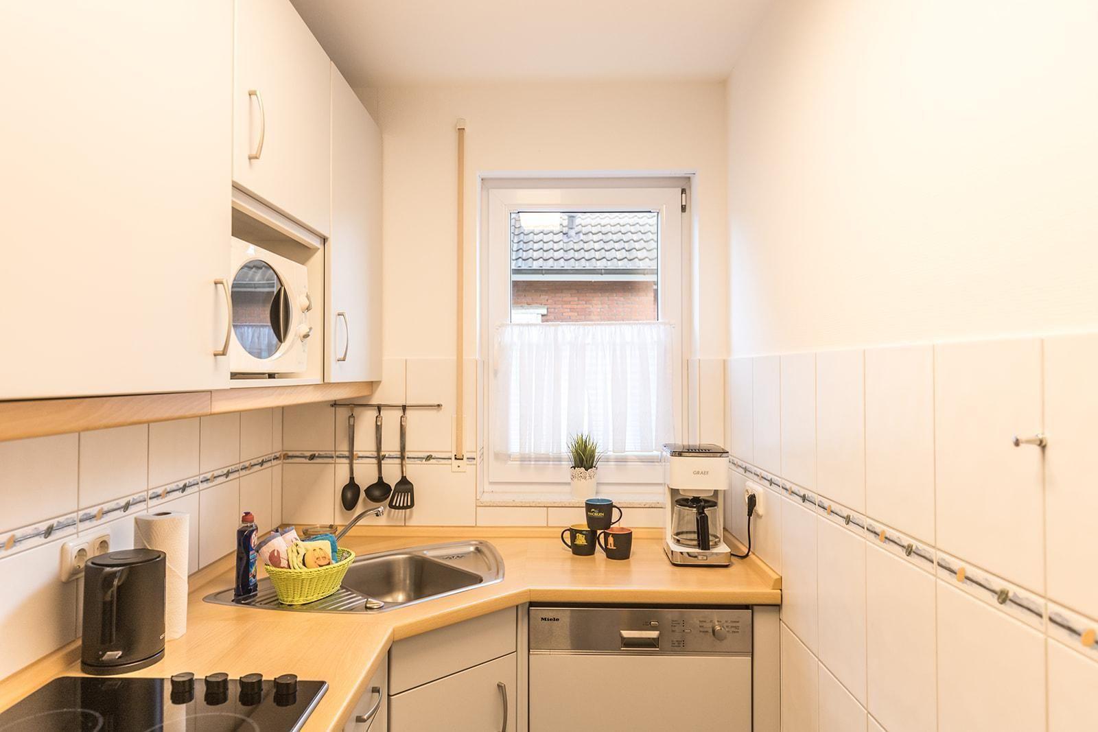 Küche mit Spüle, Herd, Kaffeemaschine und Fenster.