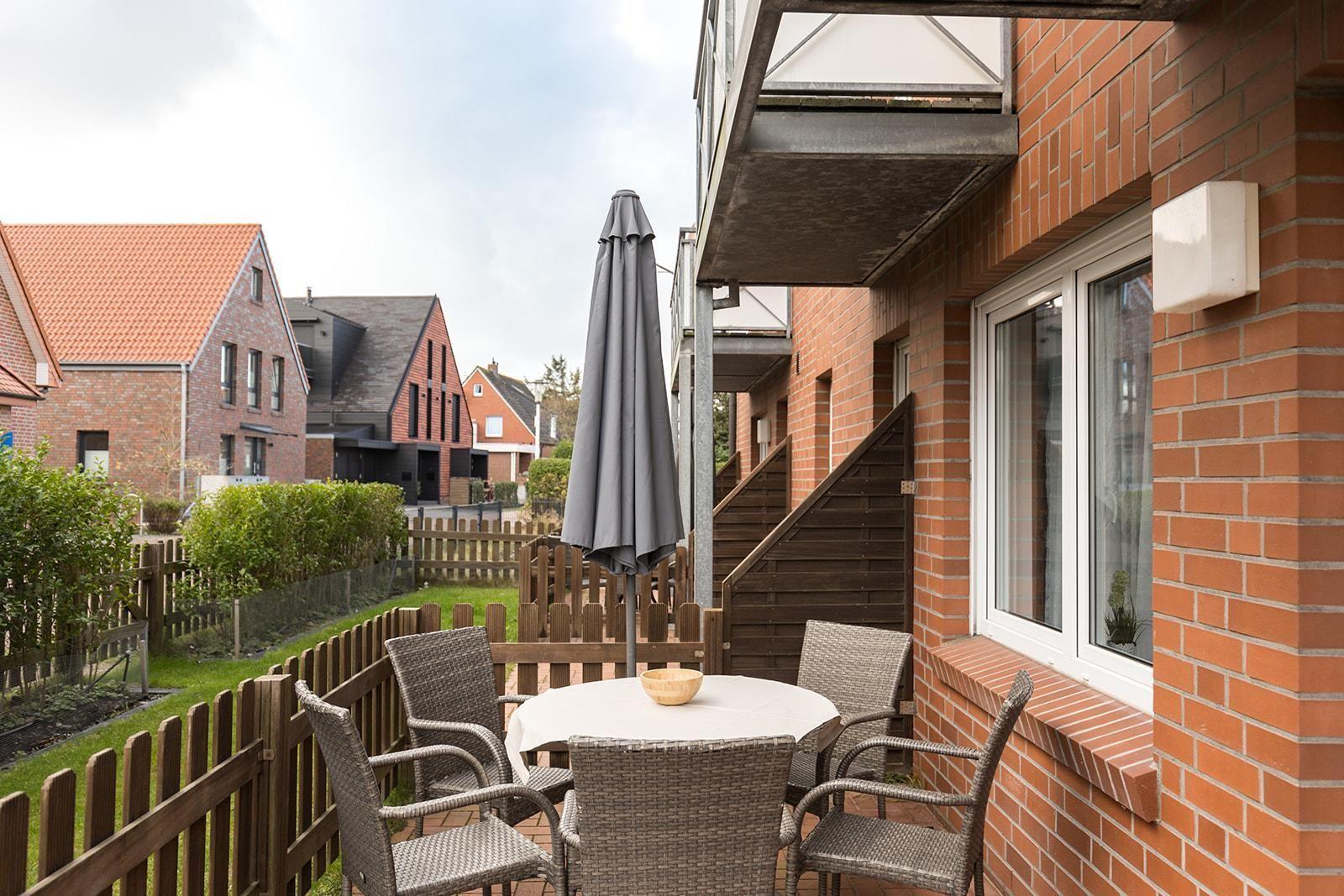 Terrasse mit Tisch, Stühlen und Schirm. Hinterhof mit Holzzaun und Grünflächen.