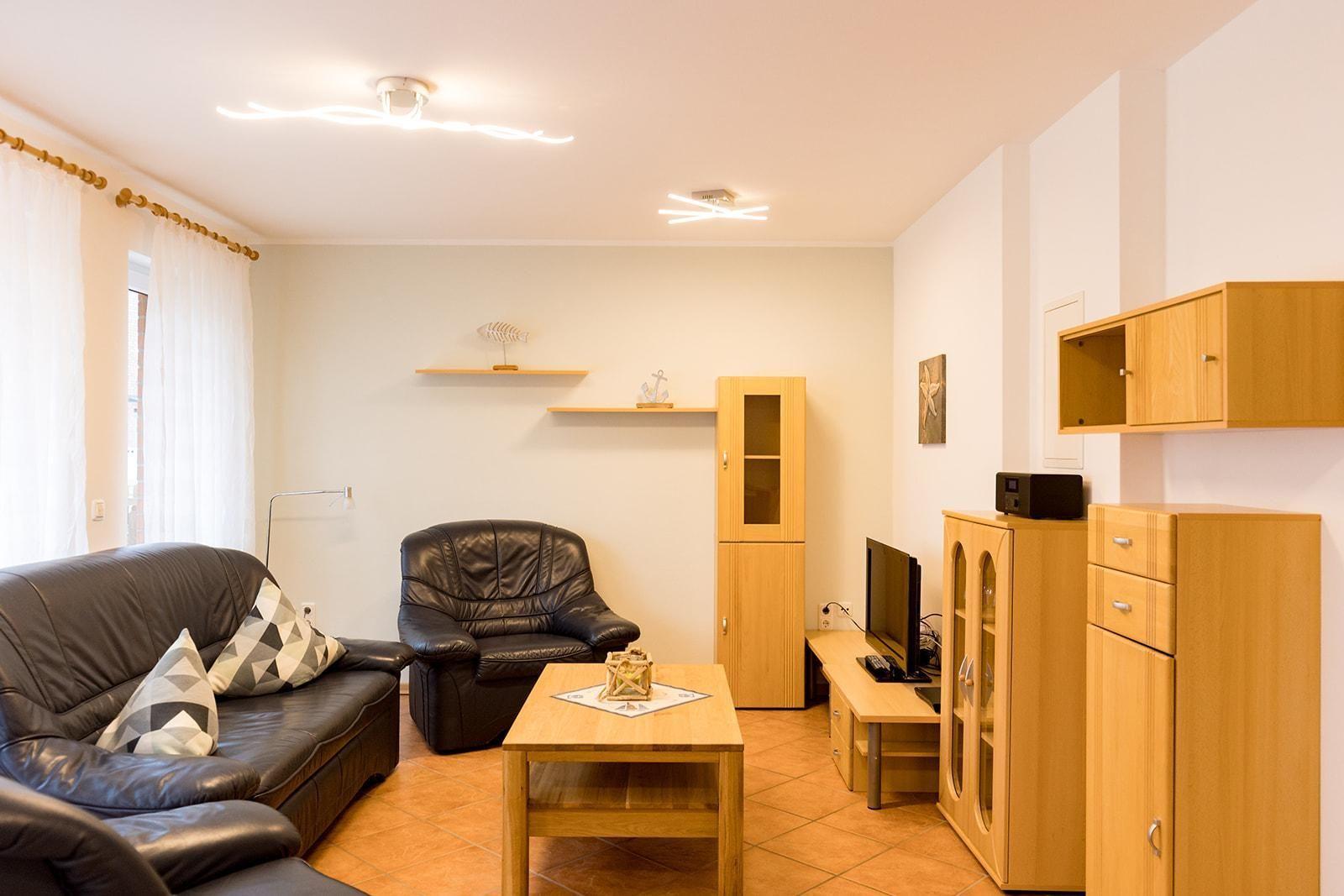 Wohnzimmer mit Ledersofa, Ledersessel, Holztisch und Holzmöbel.