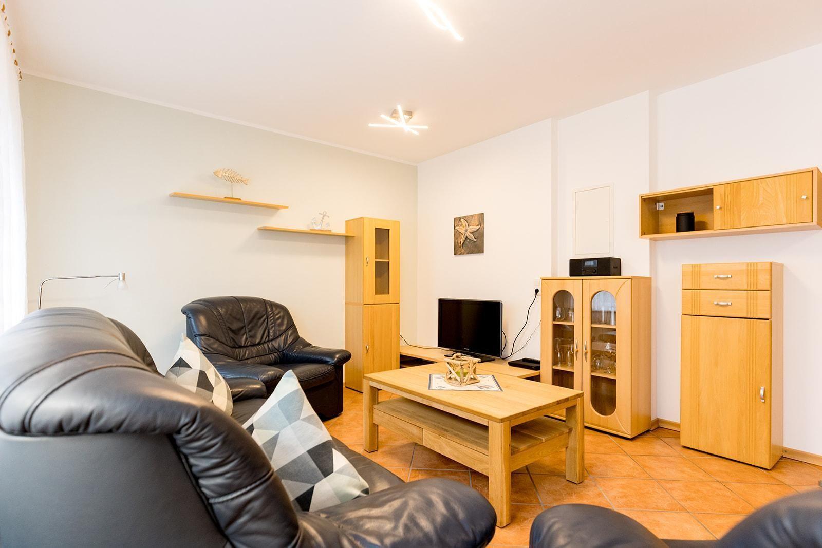 Wohnzimmer mit Ledersofa, Holztisch und Küchenschränken an der Wand.