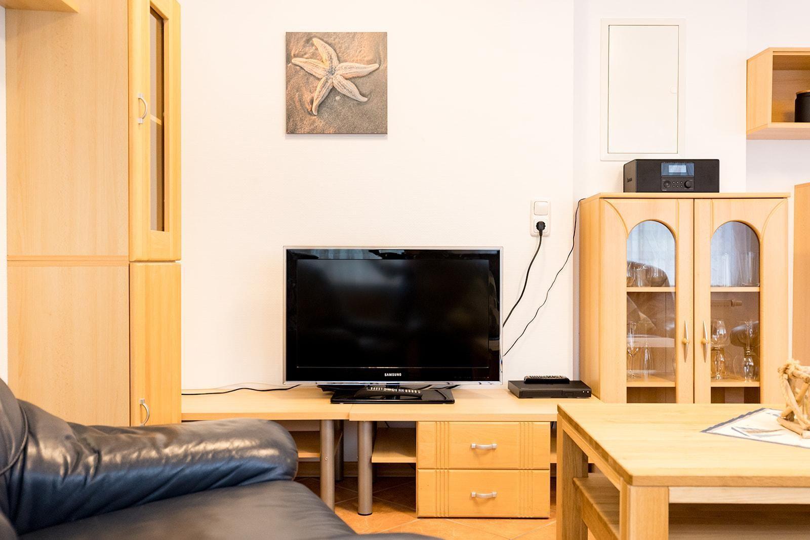 TV auf Holzregal mit Schubladen, daneben Glasvitrine und Wandbild mit Seestern.