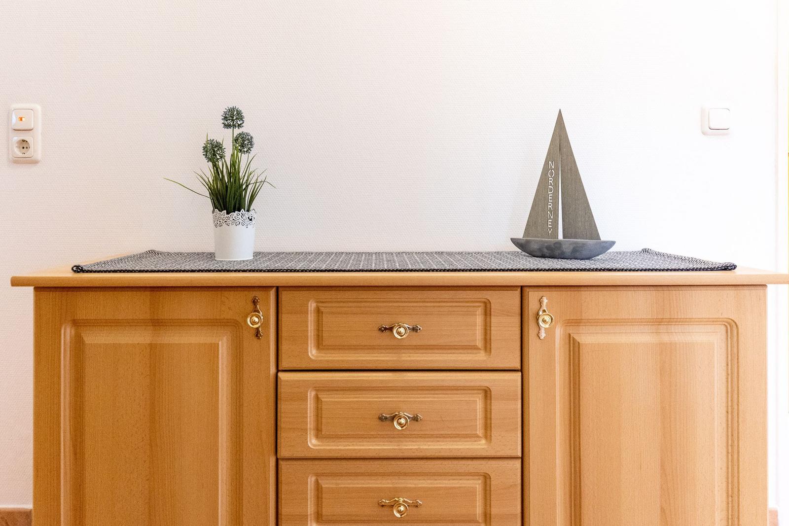 Holzschrank mit drei Schubladen und zwei Türen, darauf Pflanze und Segelschiffmodell.